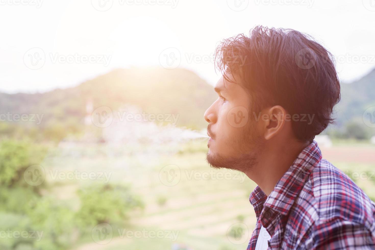 Hipster man smoking cigarette, standing behind a mountain. Among the fresh air in the morning. photo