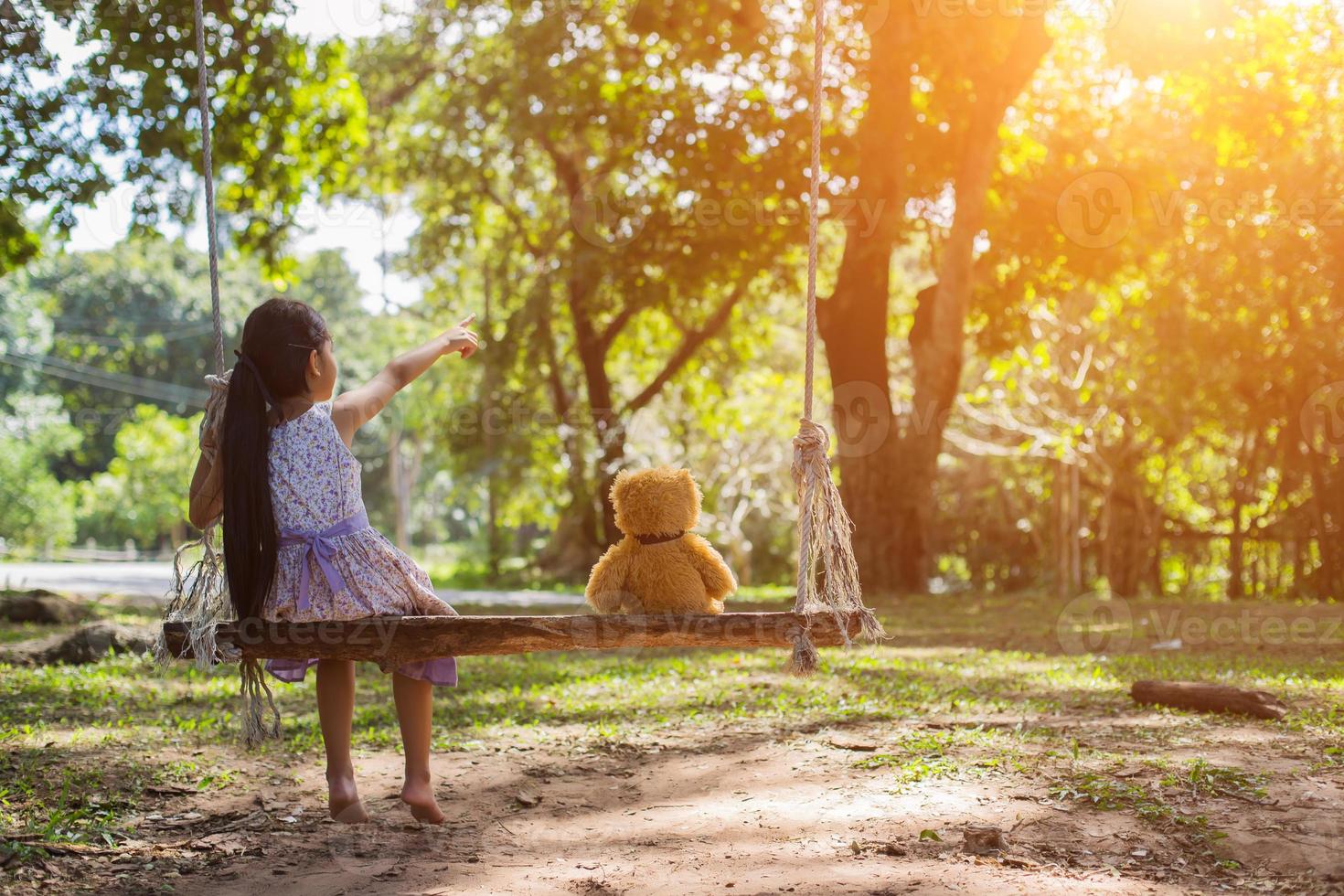 A little girl and teddy bear sitting on a swing. photo