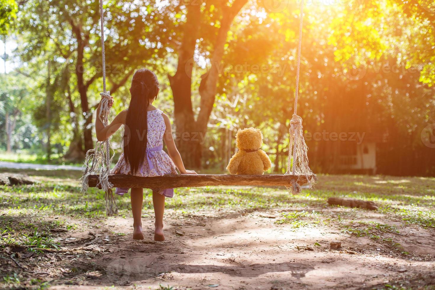 una niña y un oso de peluche sentados en un columpio. foto