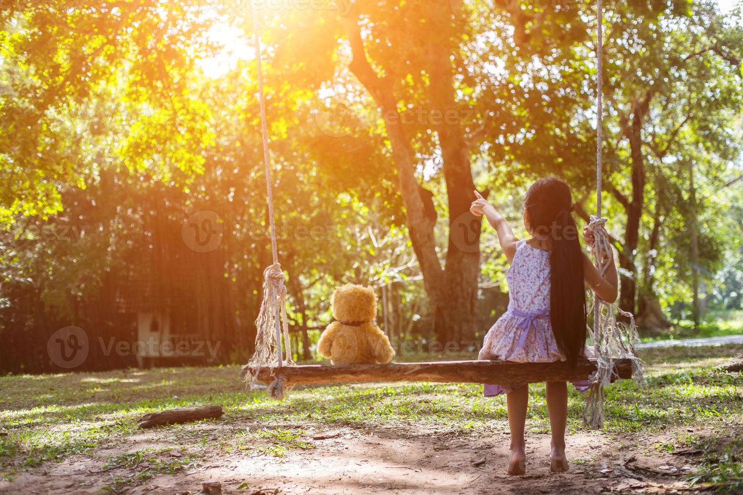 una niña y un oso de peluche sentados en un columpio. foto