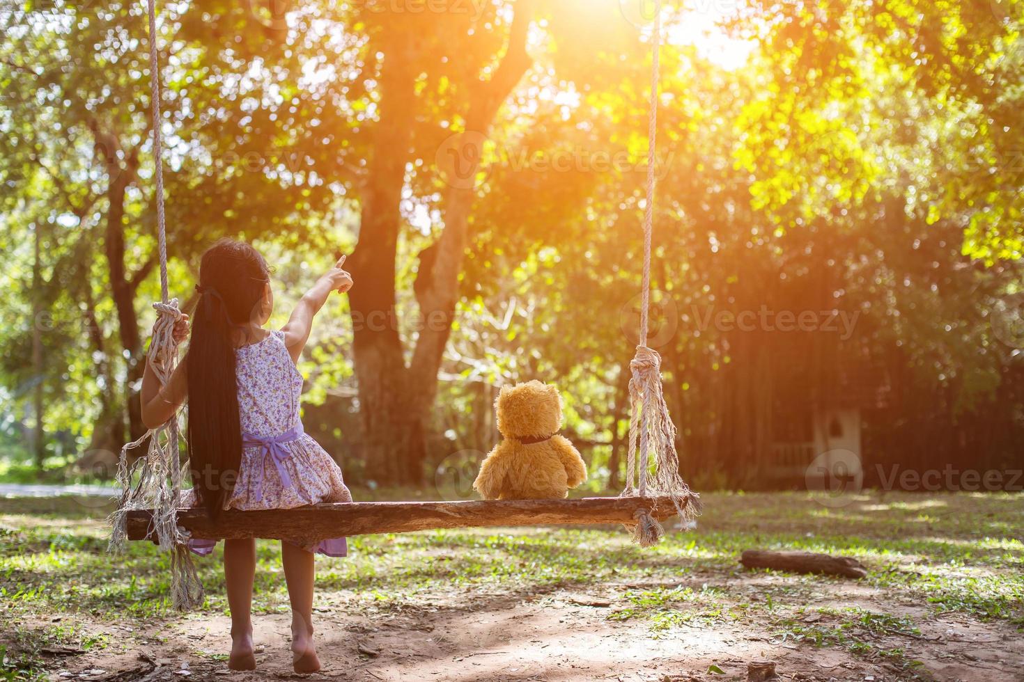 una niña y un oso de peluche sentados en un columpio. foto