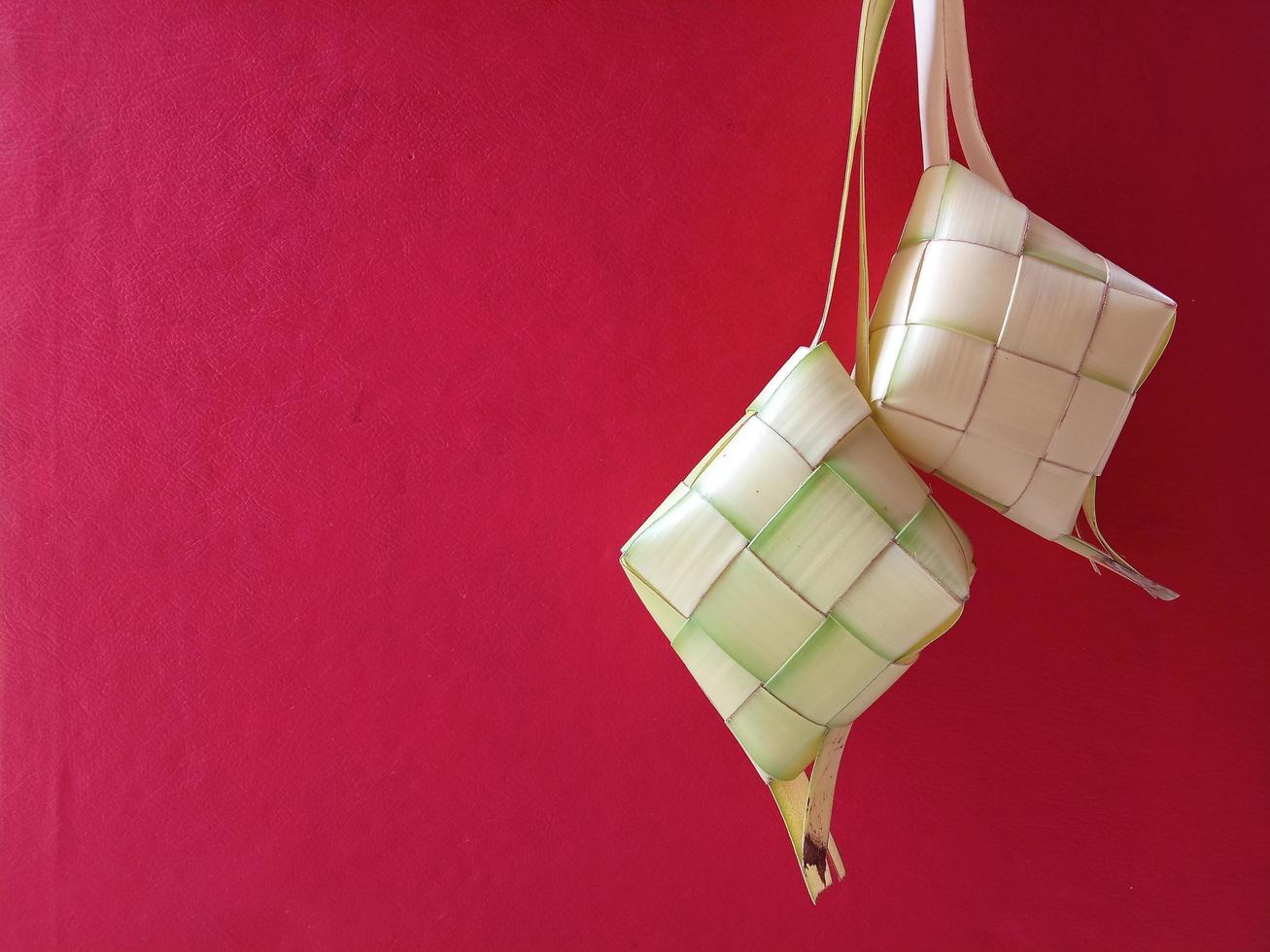Ketupat in Indonesia is a kind of way of cooking rice with coconut leaves shaped like a diamond. Usually appears on Eid al-Fitr. Conceptual photo of ketupat on red background