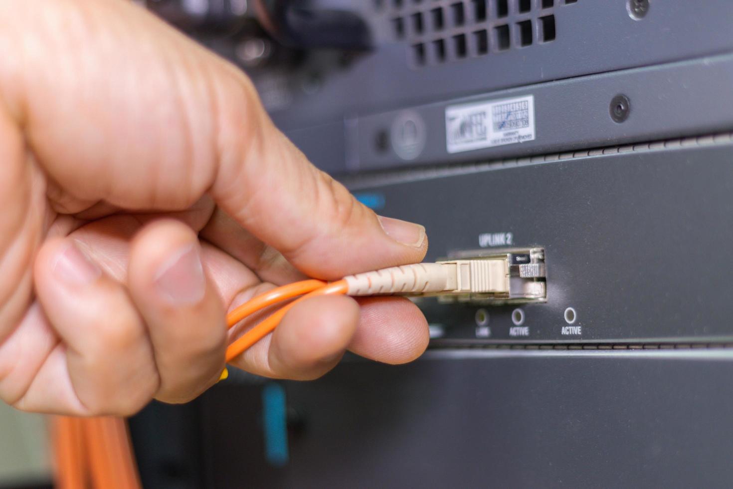 mano de un hombre que sostiene los cables de fibra óptica de la red para conectar el puerto de un interruptor para conectar la red de Internet, tecnología de comunicación conceptual foto