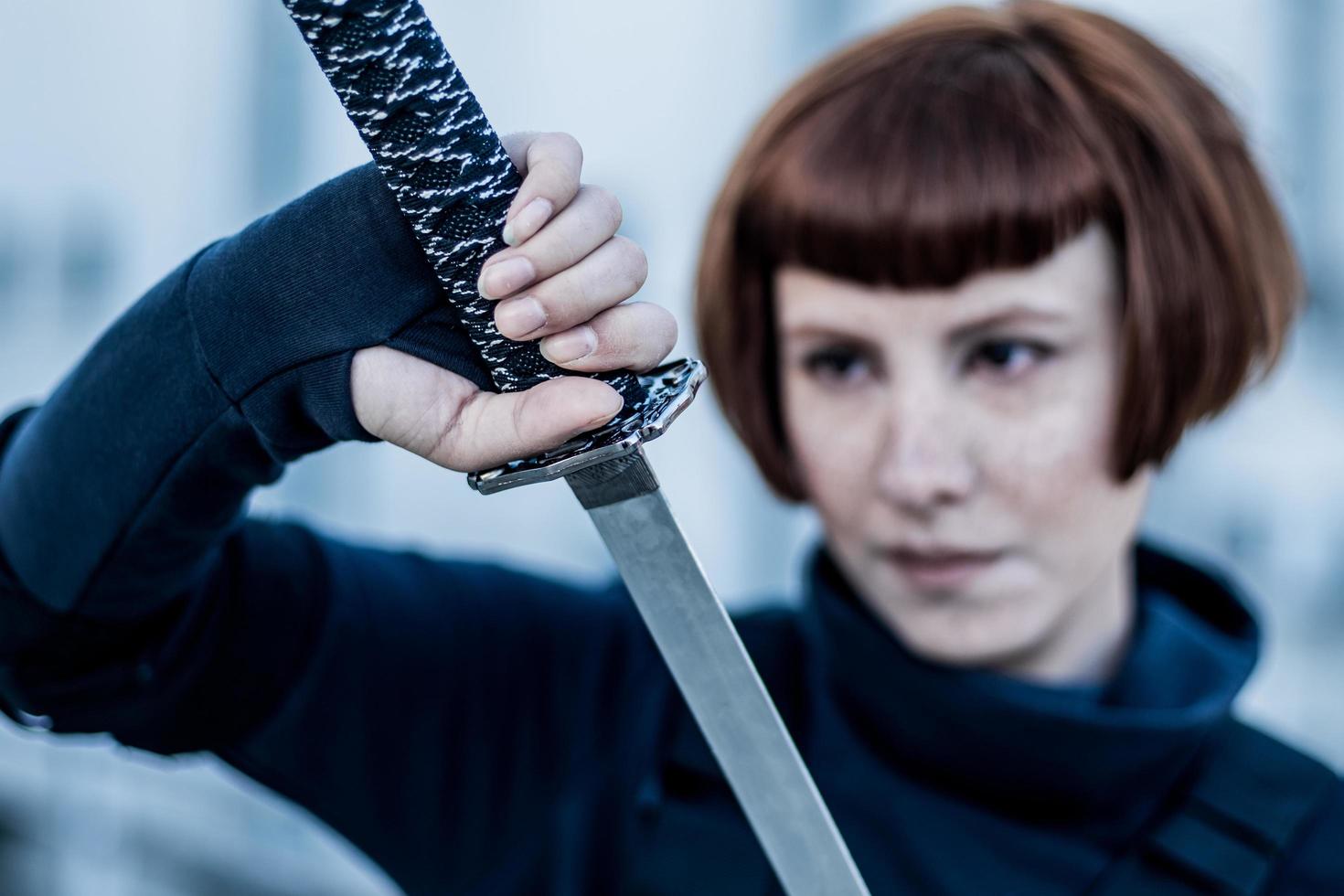 portrait of young redhead woman with japanese sword dressed in futuristic cyberpunk costume standing on the roof. photo