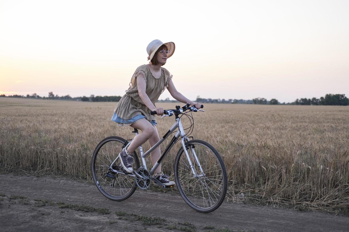 Young woman with hat ride on the bicycle in summer wheat fields photo