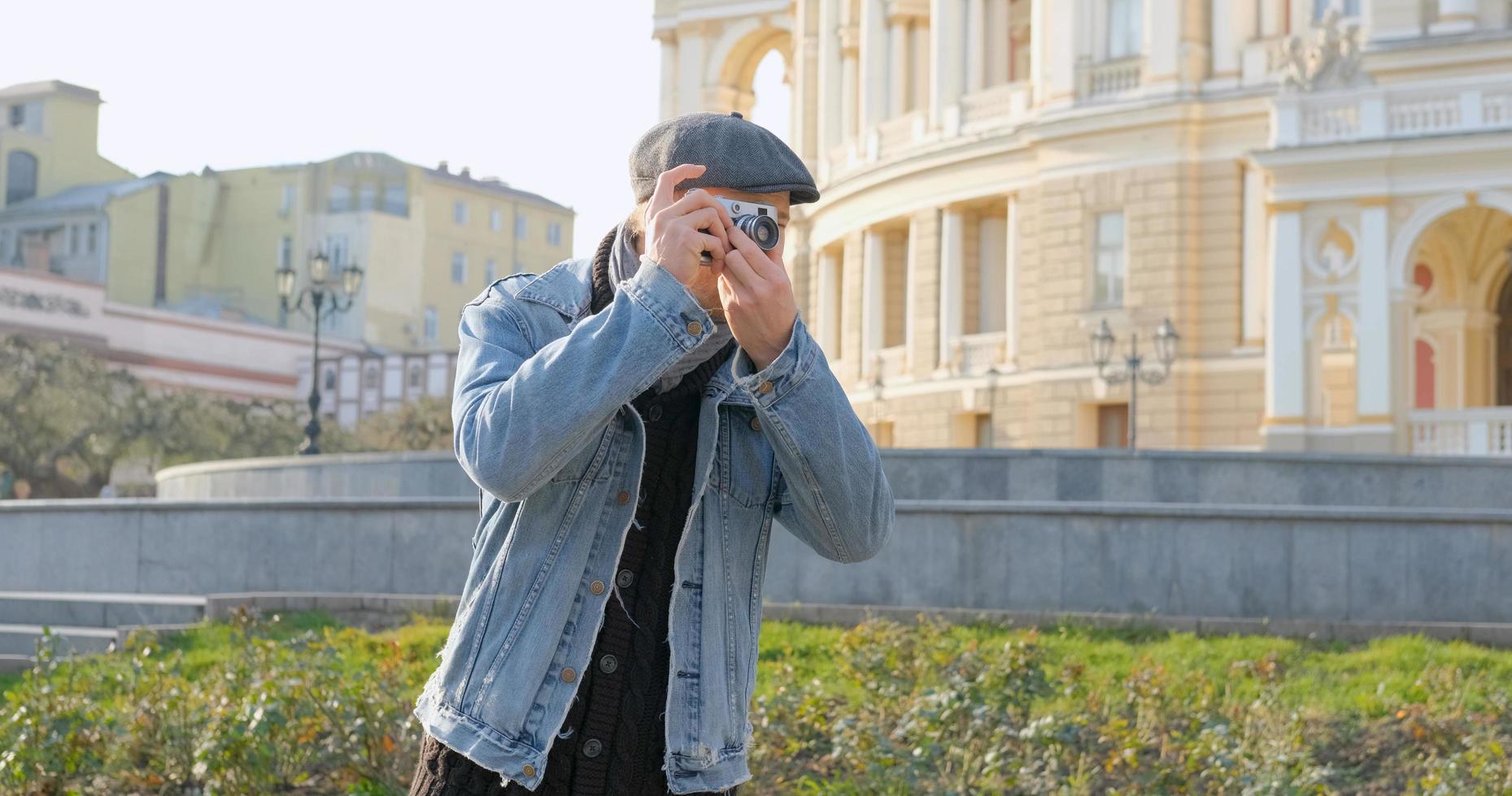 joven apuesto viajero masculino con cámara de cine hacer fotos callejeras