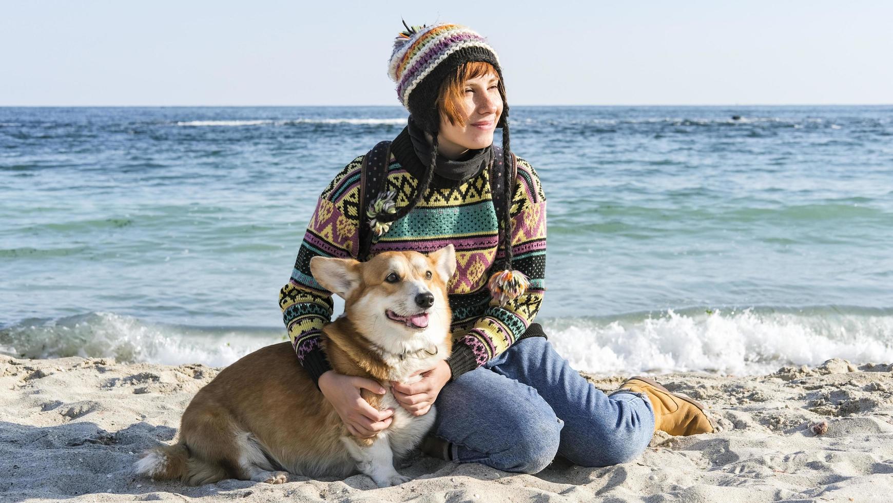 joven mujer feliz caminar con lindo perro corgi en la playa soleada de otoño foto