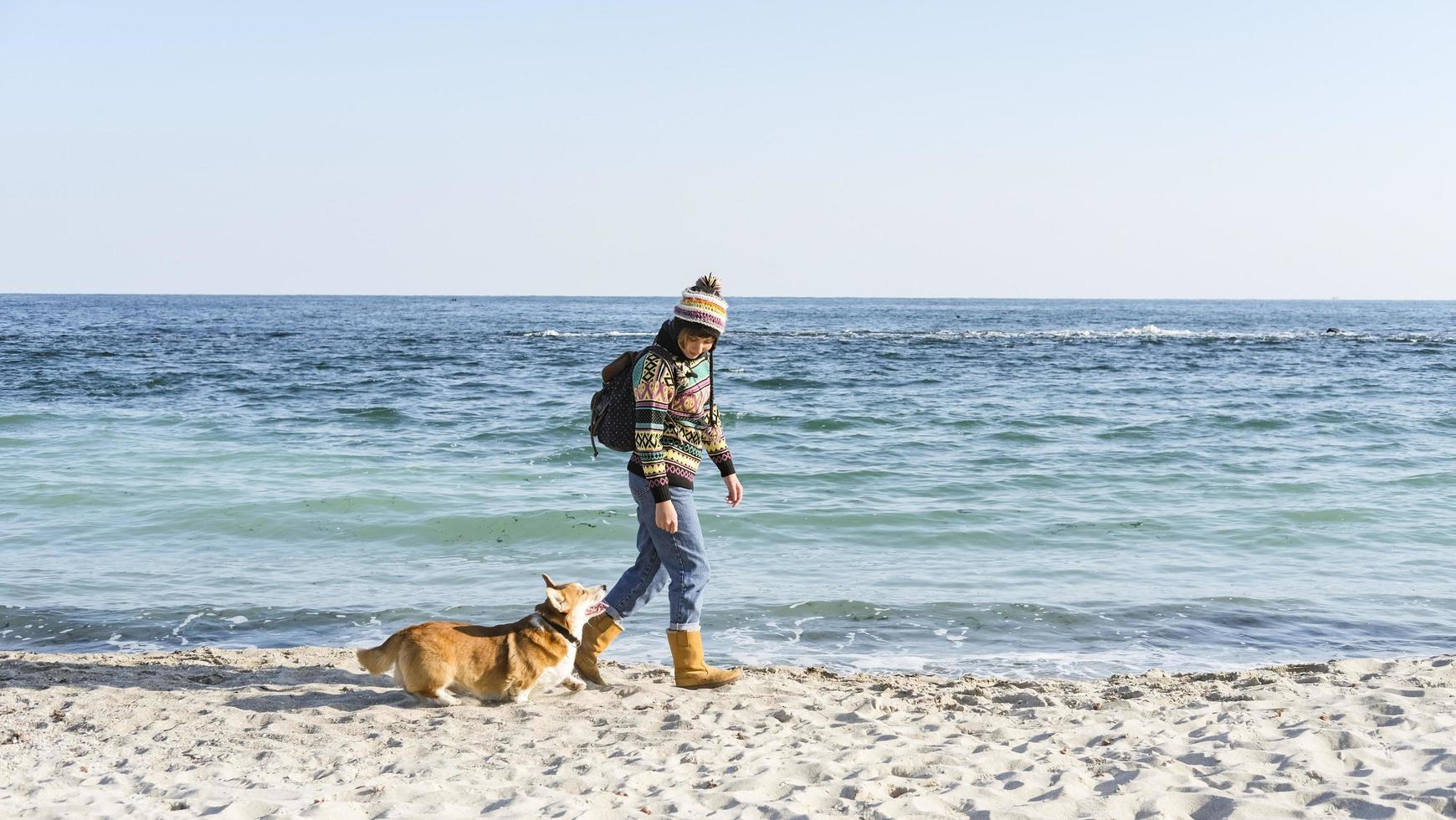 Young happy female walk with cute corgi dog on the autumn sunny beach photo