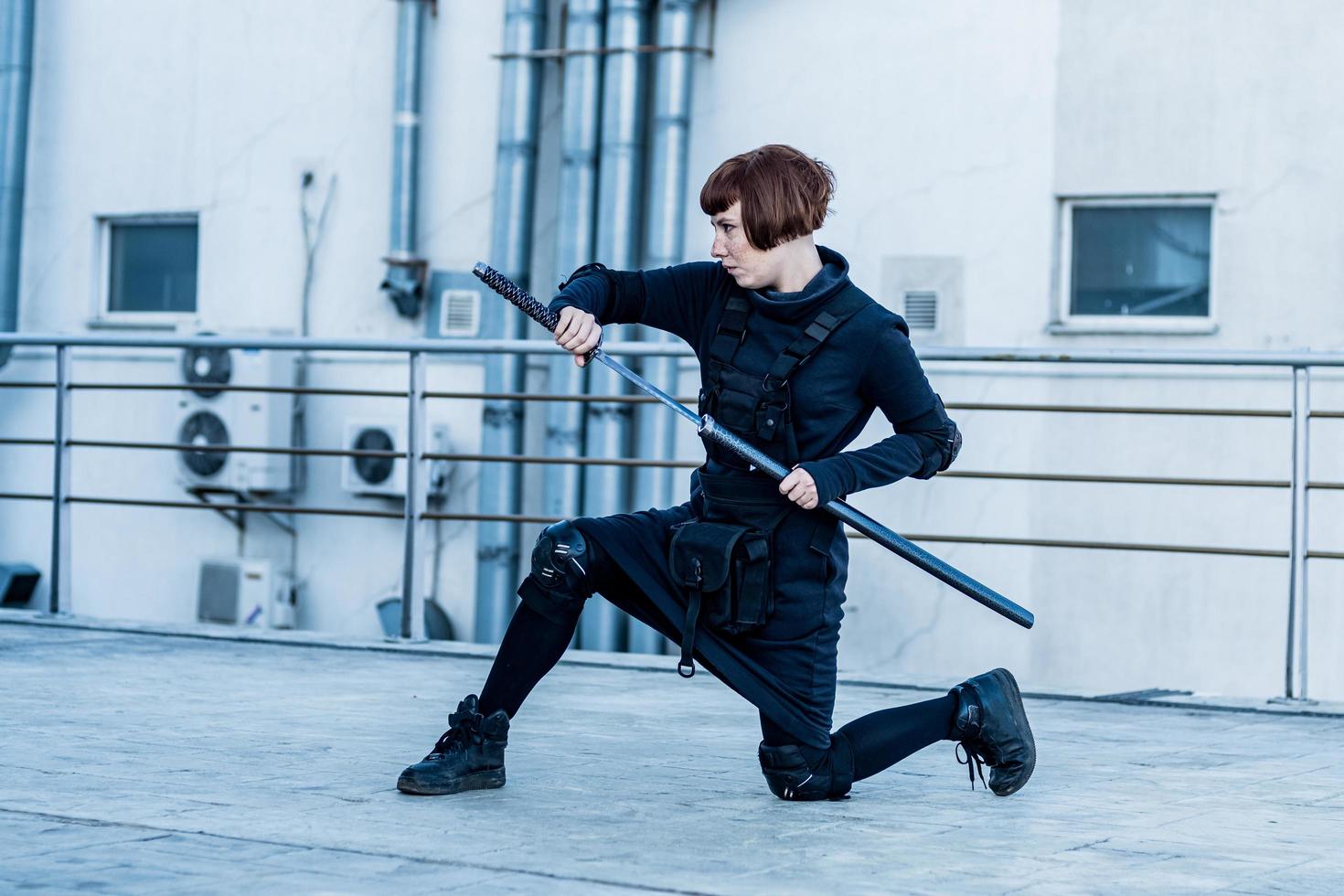 portrait of young redhead woman with japanese sword dressed in futuristic cyberpunk costume standing on the roof. photo