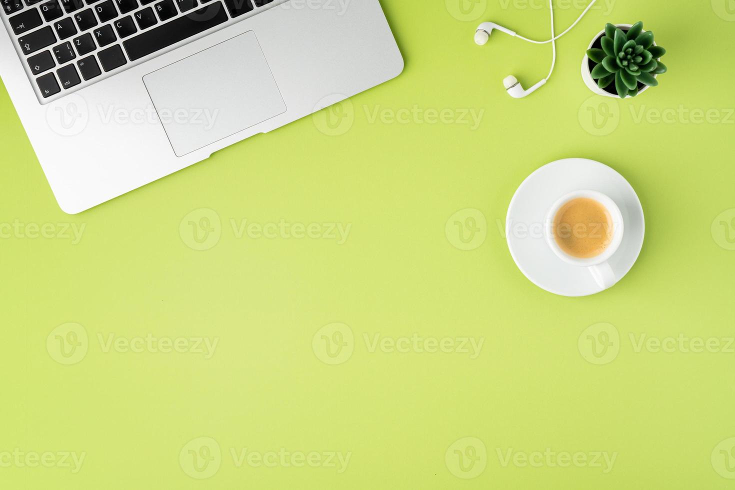 Horizontal of metallic laptop keyboard, white earphones and coffee cup on light green background photo