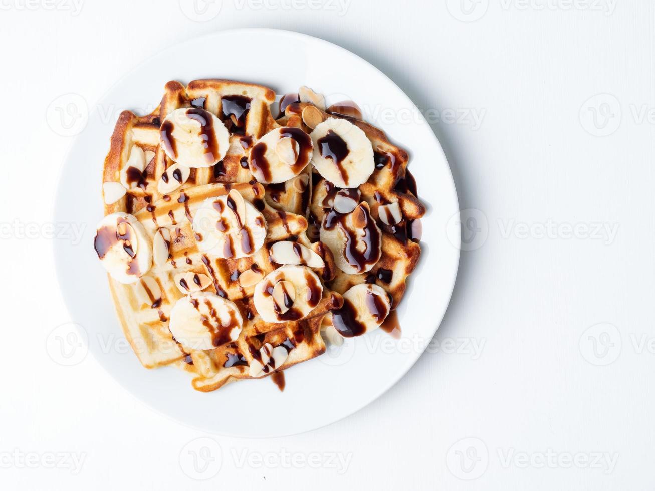 Belgian curd waffles with raspberries, banana, chocolate syrup. Breakfast with tea on white background, top view, copy space photo