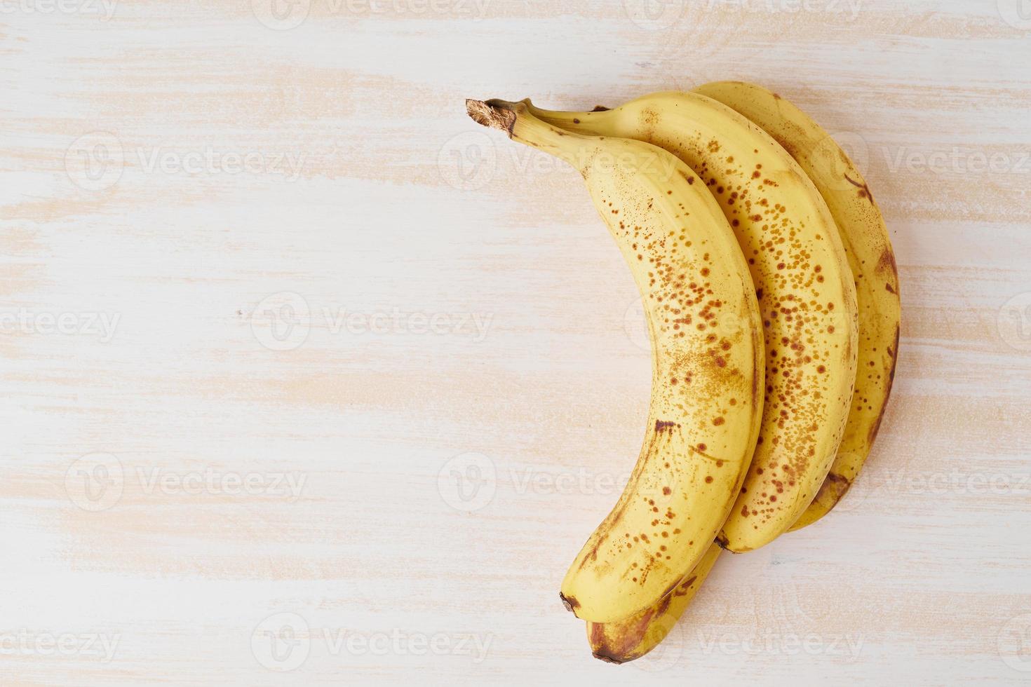 Ripe bananas with brown spots on bright white wooden table, copy space, top view photo