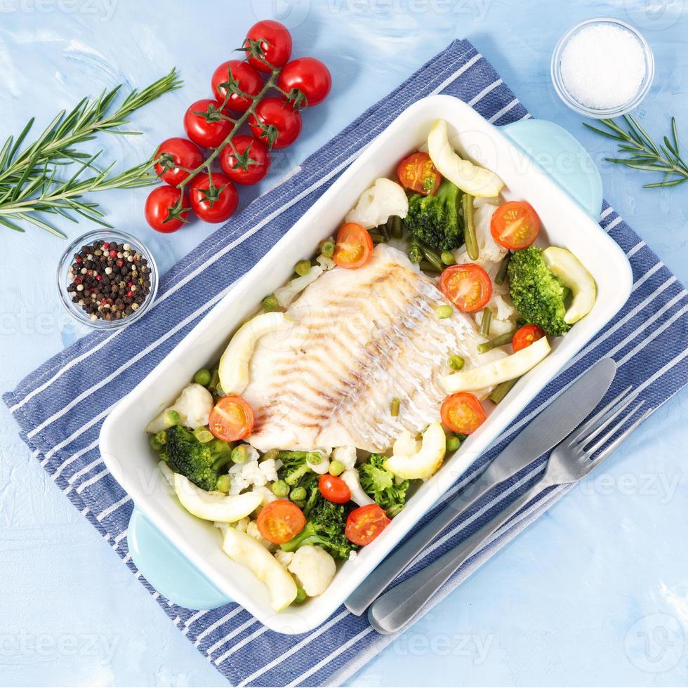 Fish cod baked in blue oven with vegetables - broccoli, tomatoes. Healthy diet food. Blue stone background, top view. photo