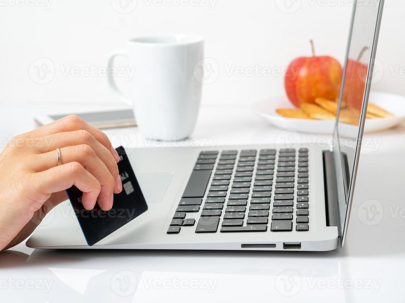 mujer sentada en la mesa en casa y mirando la computadora portátil, paga las compras con tarjeta de crédito, en línea foto