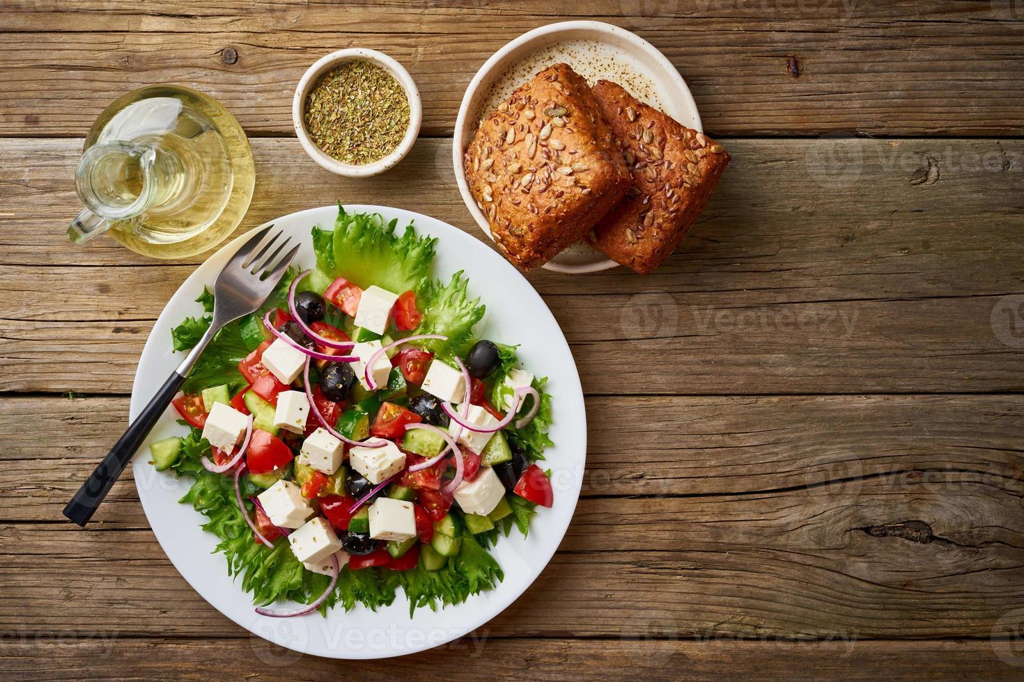 Greek salad on white plate on old rustic wooden table, top view, copy space photo