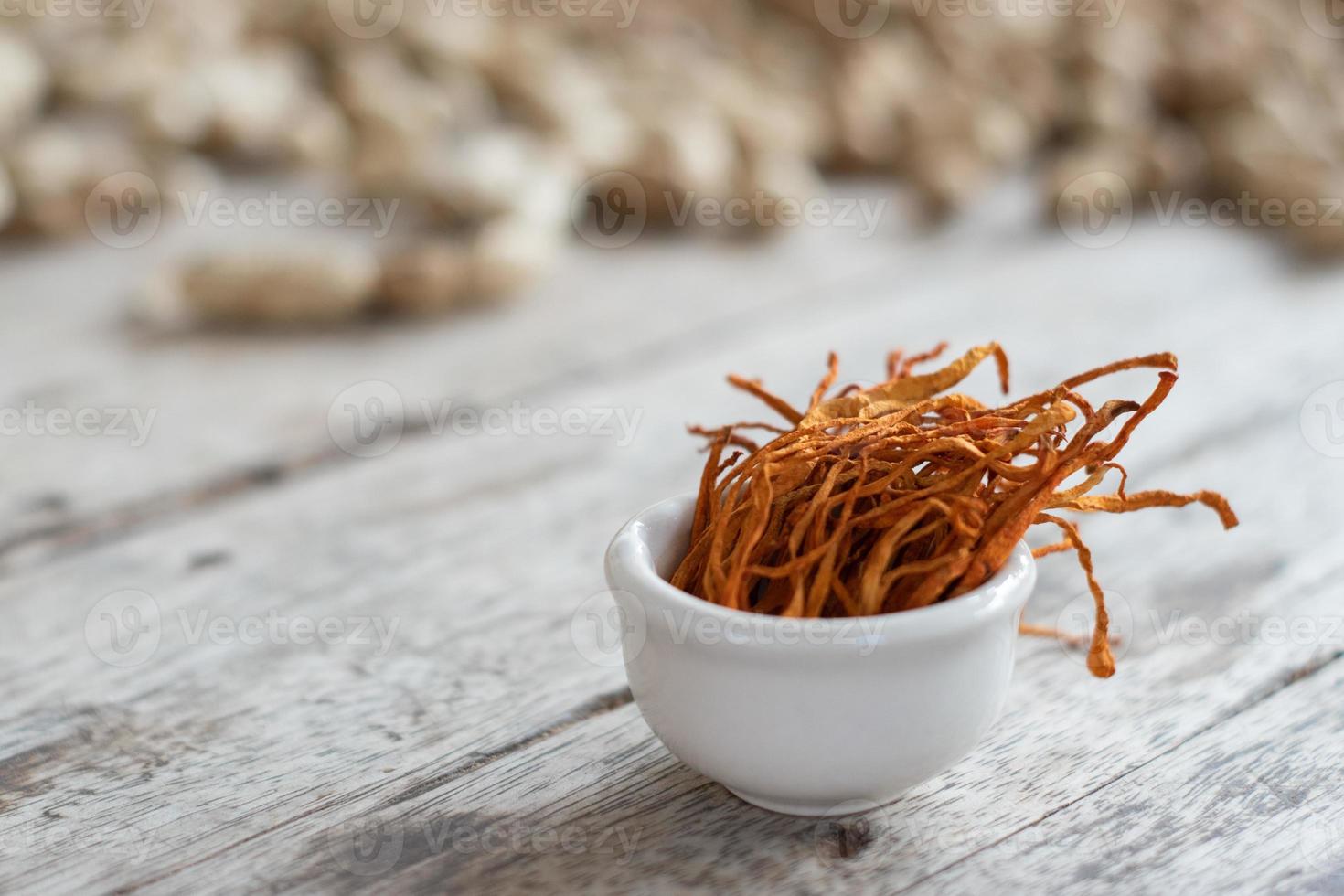 Dry cordyceps militaris mycelium in white bowl with wooden background. Orange medical mushroom for good health. photo