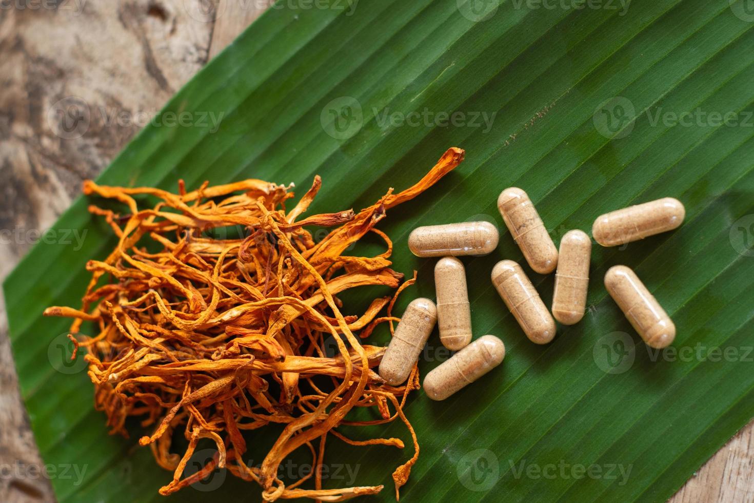 Dry cordyceps militaris on a green banana leaf with wooden background. Orange medical mushroom for good health with capsules. photo