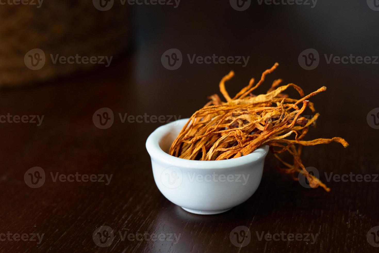 Dry cordyceps militaris mycelium in white bowl with wooden background. Orange medical mushroom for good health. photo