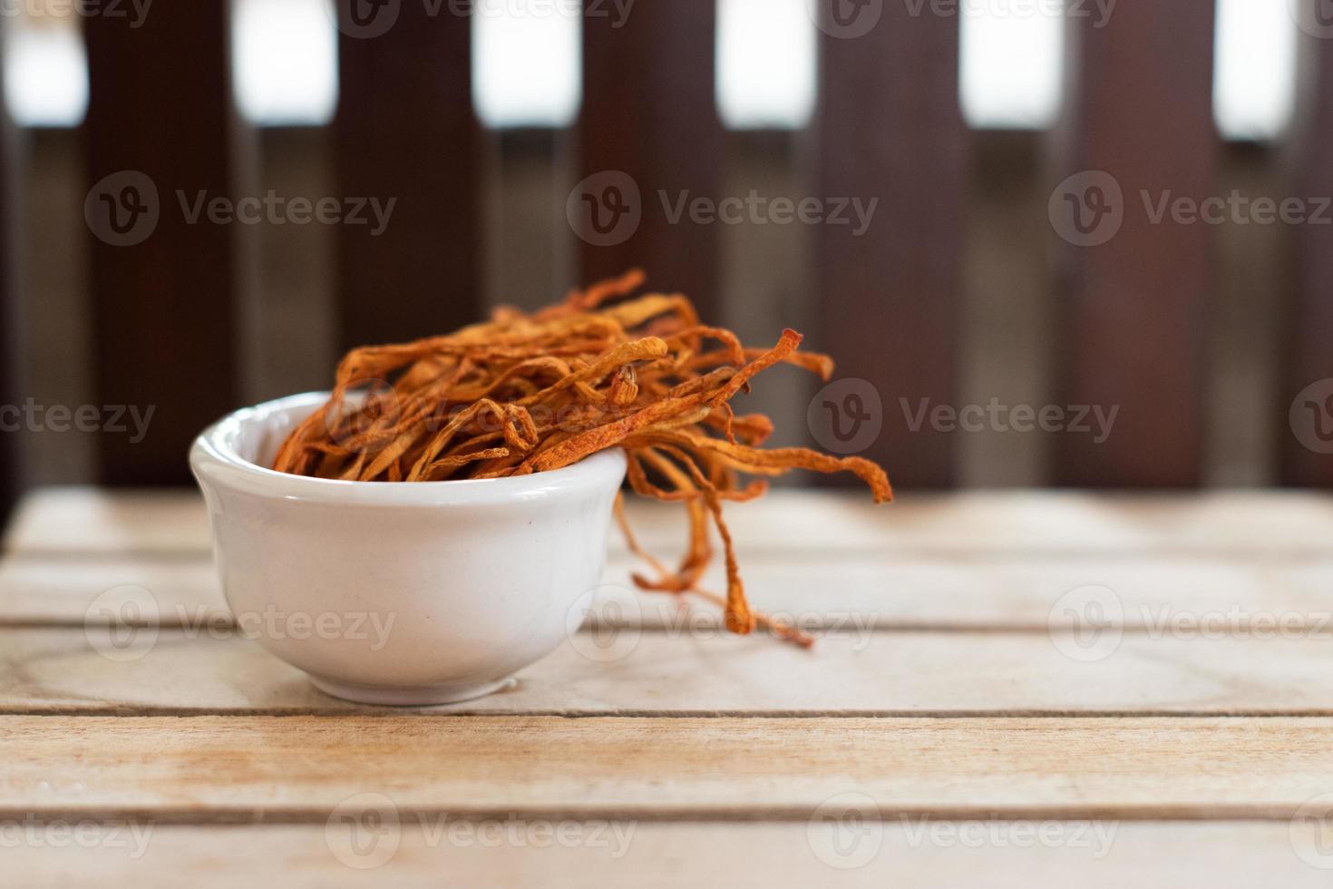 Dry cordyceps militaris mycelium in white bowl with wooden background. Orange medical mushroom for good health. photo