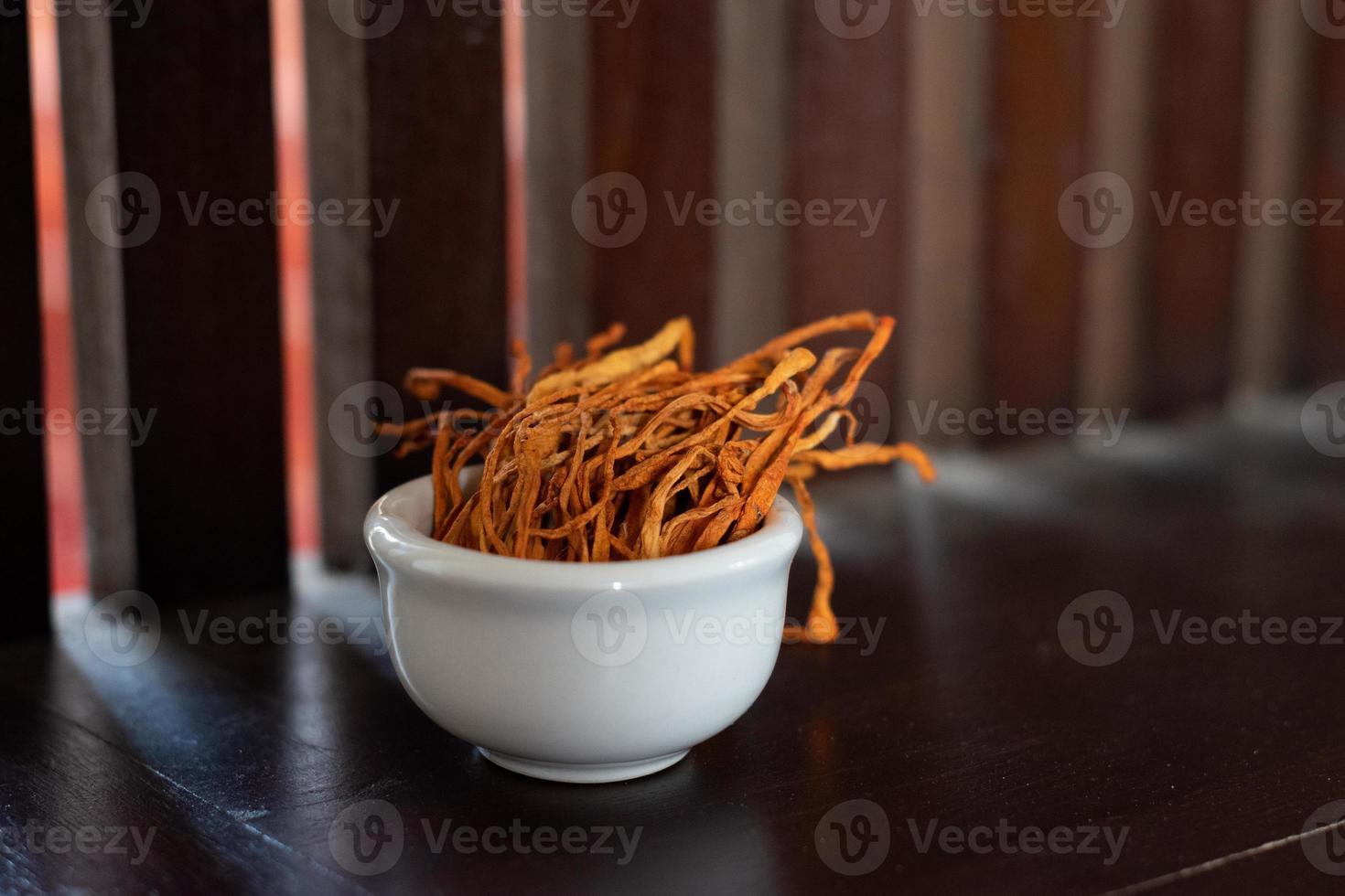 Dry cordyceps militaris mycelium in white bowl with wooden background. Orange medical mushroom for good health. photo