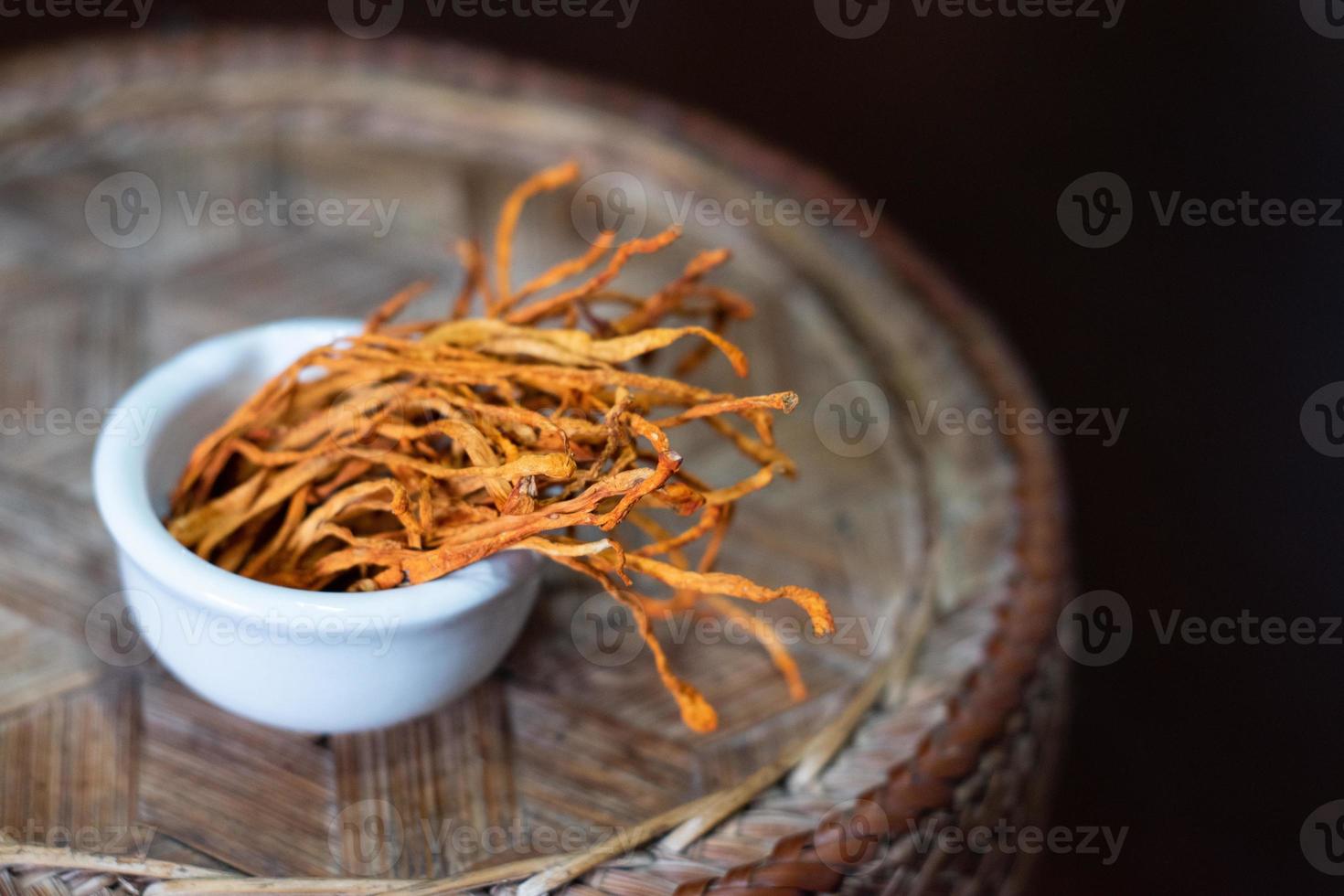 Dry cordyceps militaris mycelium in white bowl with wooden background. Orange medical mushroom for good health. photo