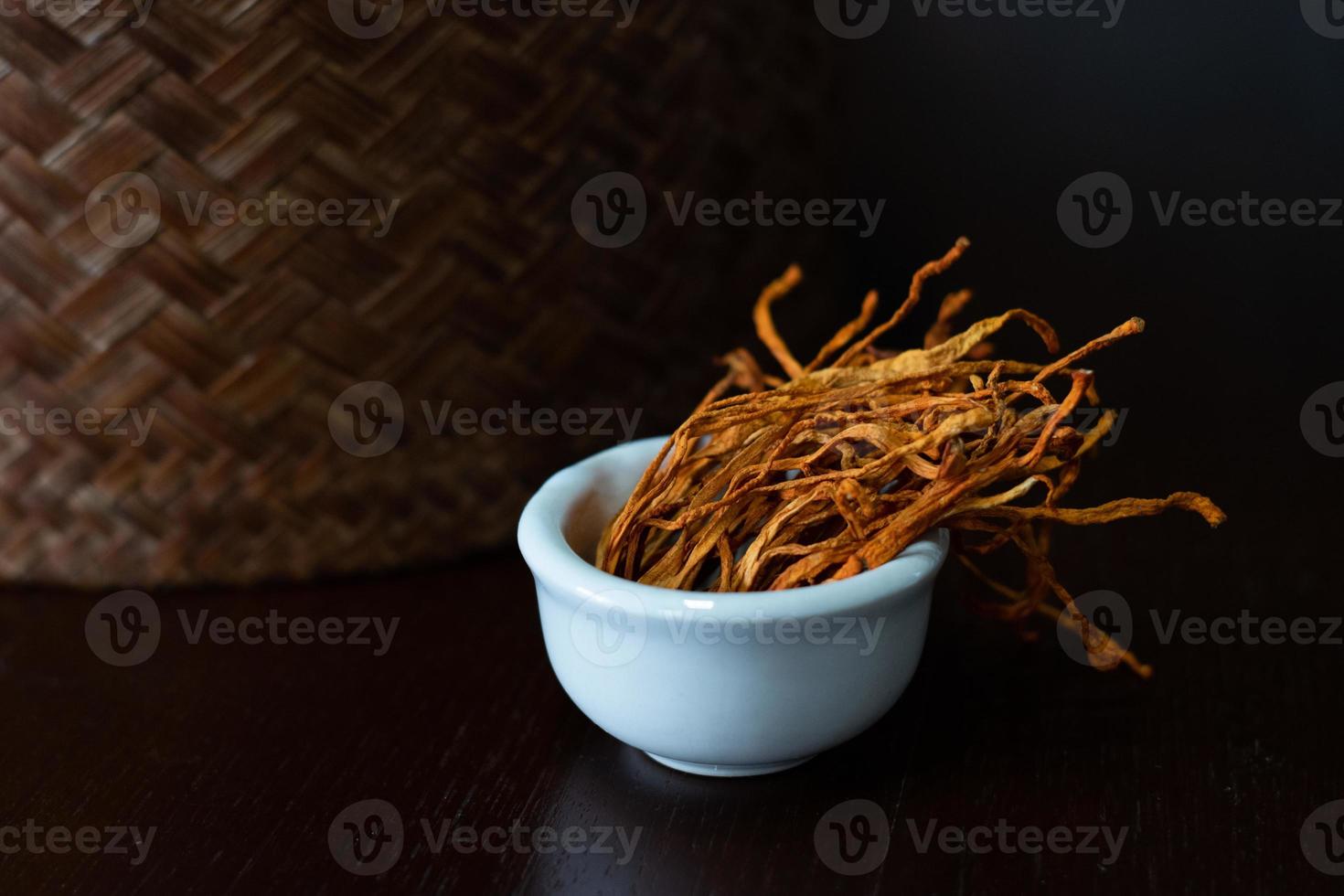 Dry cordyceps militaris mycelium in white bowl with wooden background. Orange medical mushroom for good health. photo