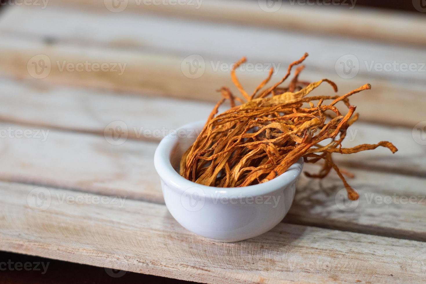 Dry cordyceps militaris mycelium in white bowl with wooden background. Orange medical mushroom for good health. photo