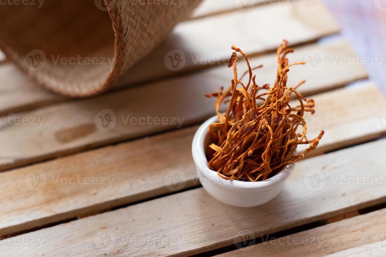 Dry cordyceps militaris mycelium in white bowl with wooden background. Orange medical mushroom for good health. photo