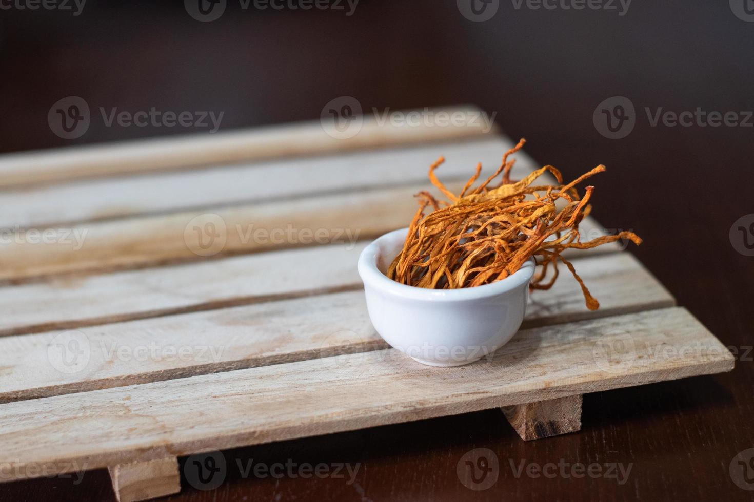 Dry cordyceps militaris mycelium in white bowl with wooden background. Orange medical mushroom for good health. photo