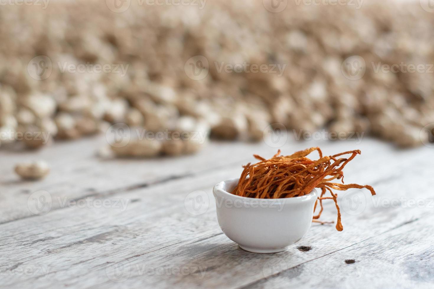 Dry cordyceps militaris mycelium in white bowl with wooden background. Orange medical mushroom for good health. photo