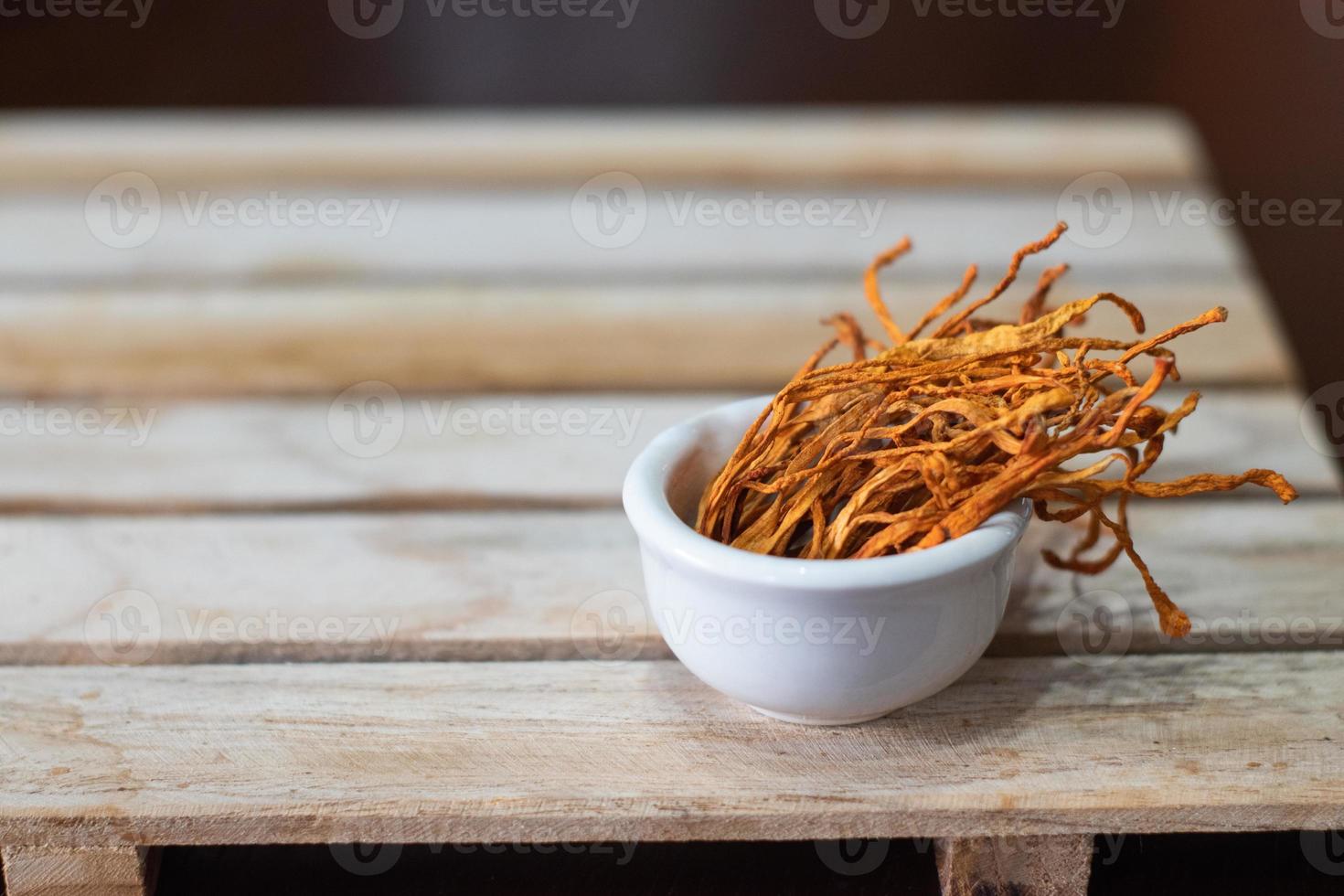 Dry cordyceps militaris mycelium in white bowl with wooden background. Orange medical mushroom for good health. photo