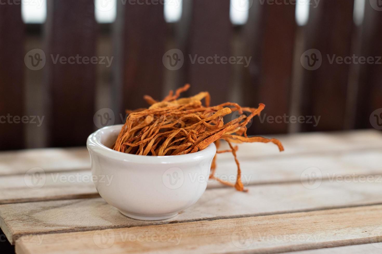 Dry cordyceps militaris mycelium in white bowl with wooden background. Orange medical mushroom for good health. photo