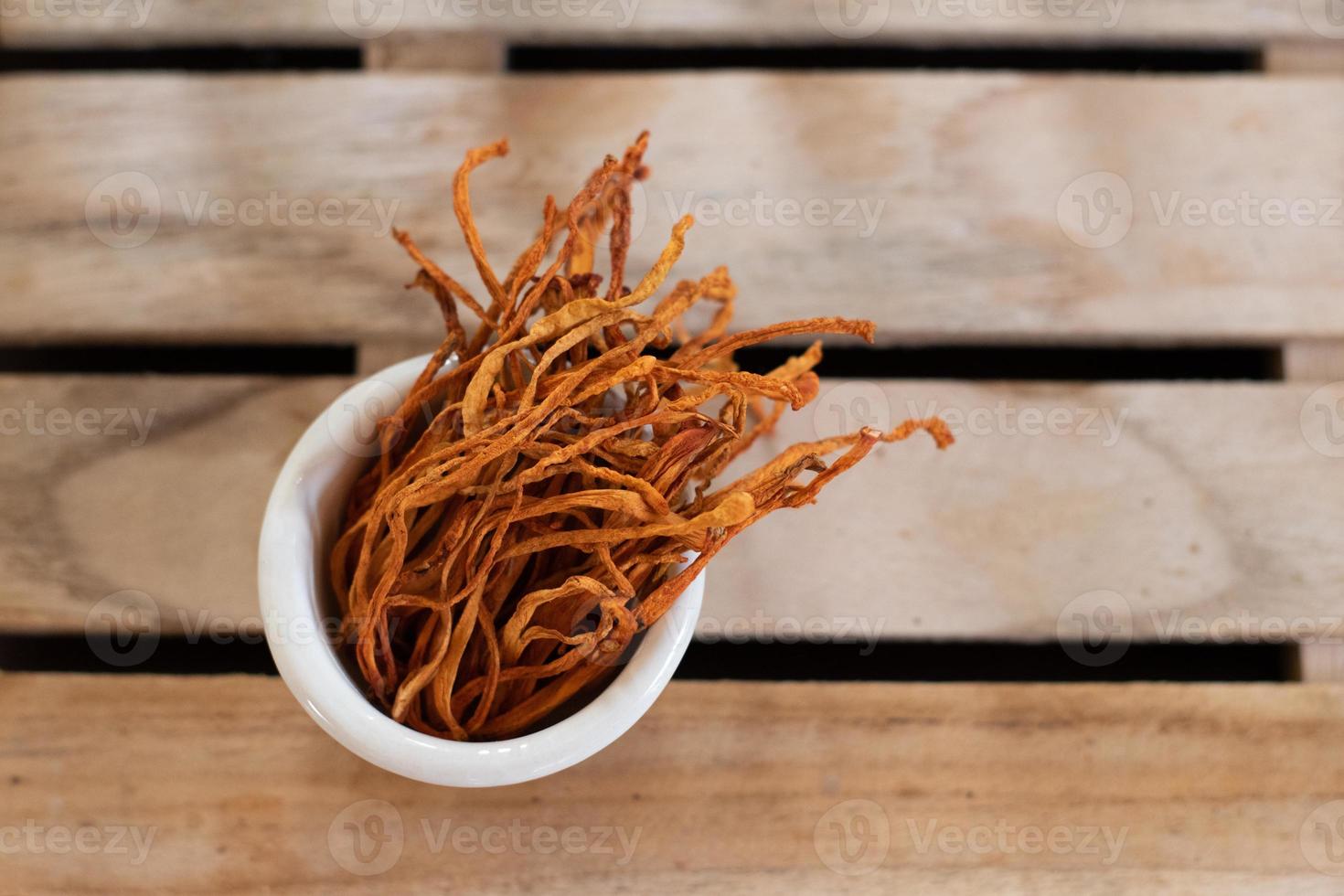 Dry cordyceps militaris mycelium in white bowl with wooden background. Orange medical mushroom for good health. photo