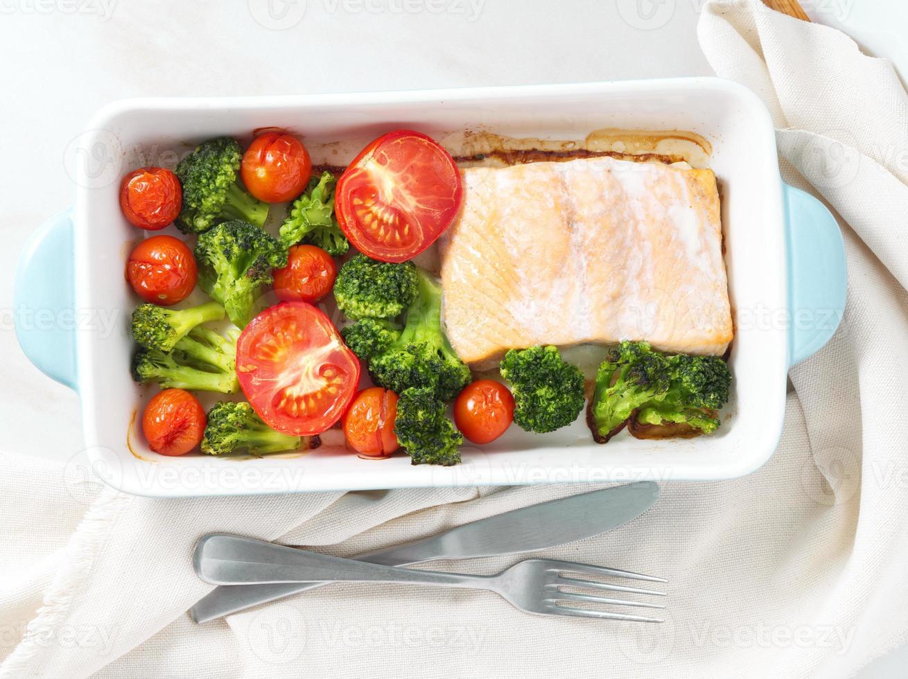 Fish salmon baked in oven with vegetables - broccoli, tomatoes. Healthy diet food, white marble backdrop, top view. photo