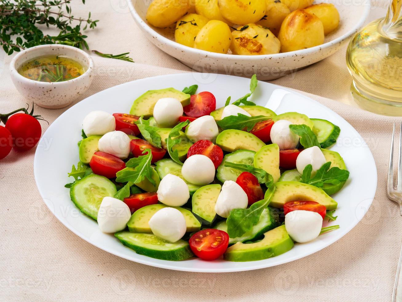 ensalada fresca con tomates, pepinos, rúcula, mozzarella y aguacate. aceite con especias, foto