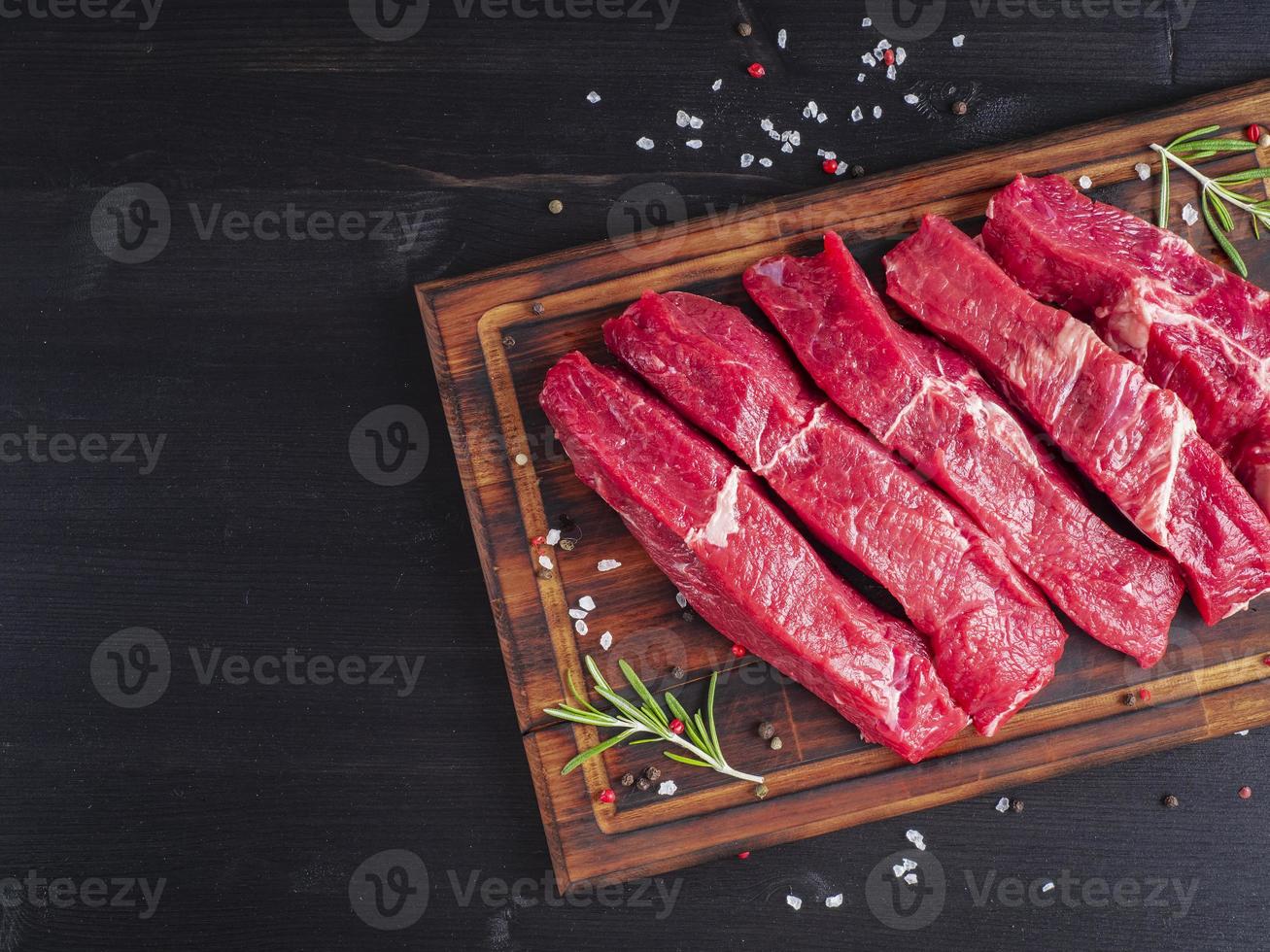 Raw meat, beef steak with seasoning on chopping board on dark background with rosemary, photo