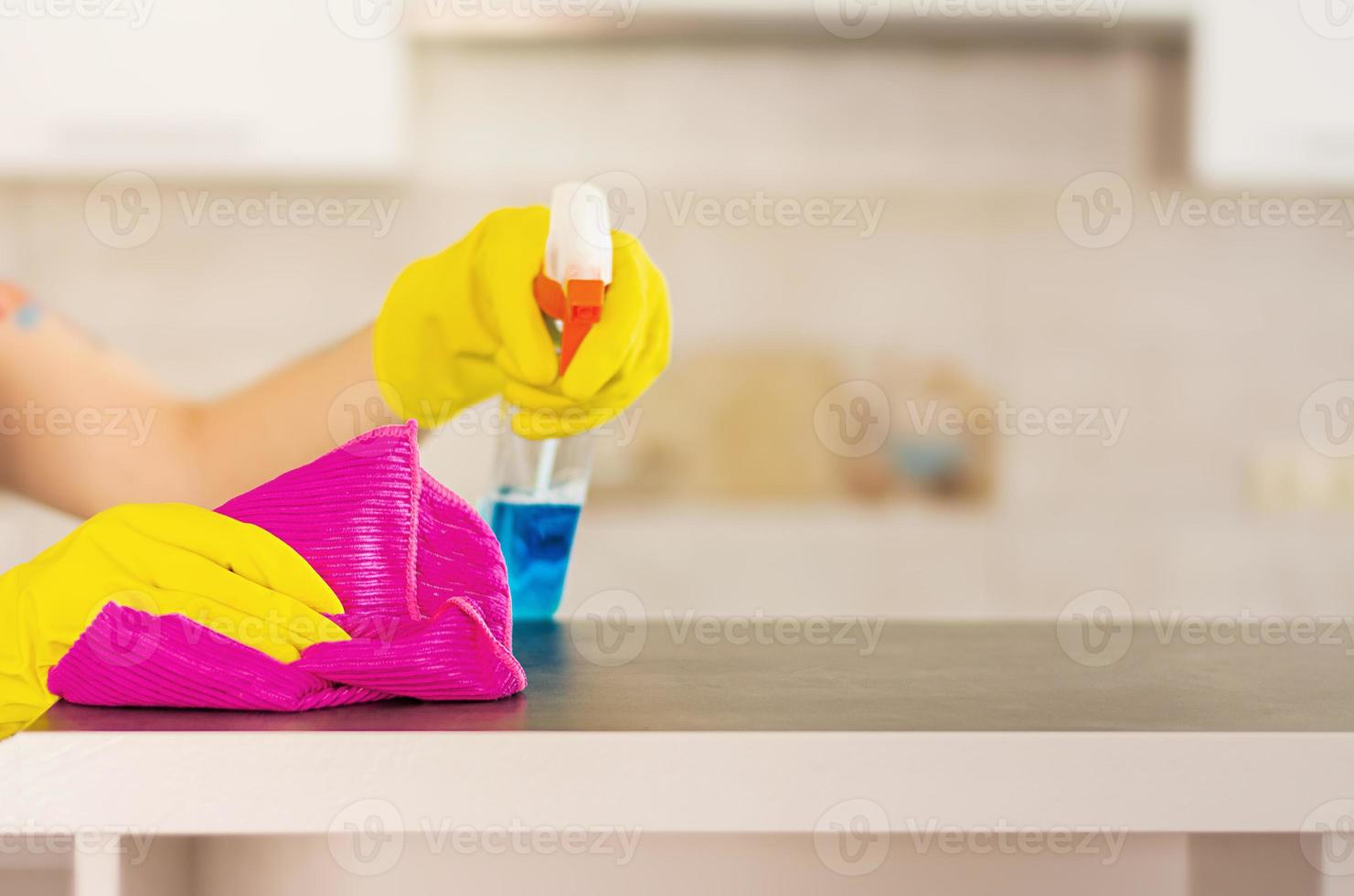 Woman in protective gloves wiping dust using cleaning spray and duster. Cleaning service concept. photo