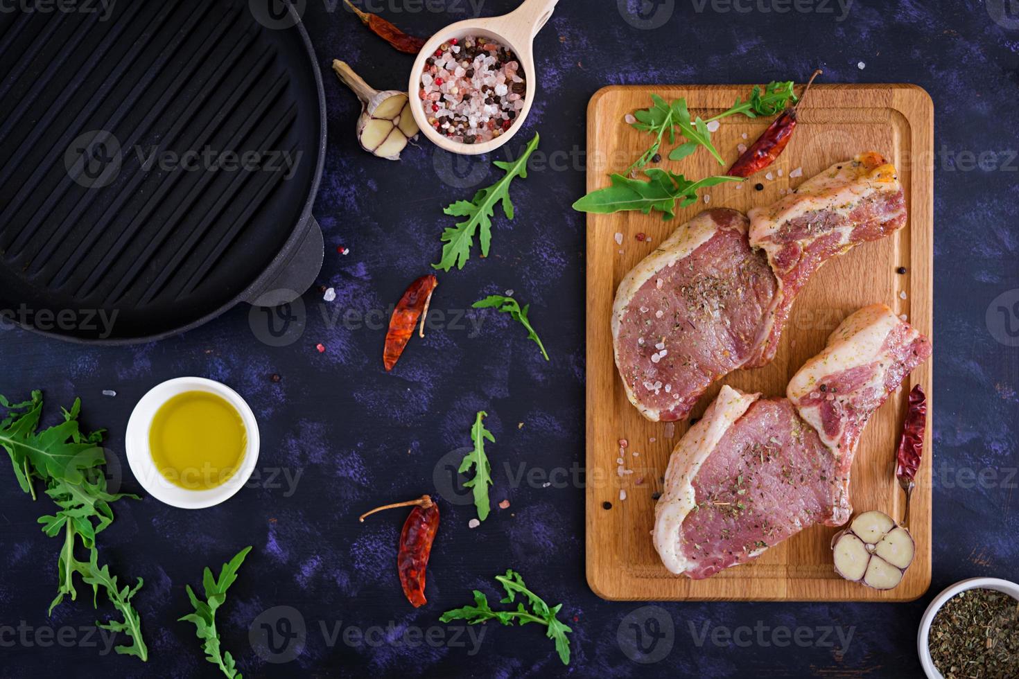 Raw pork steak with herbs on dark background. Raw juicy steak on bone. Top view photo