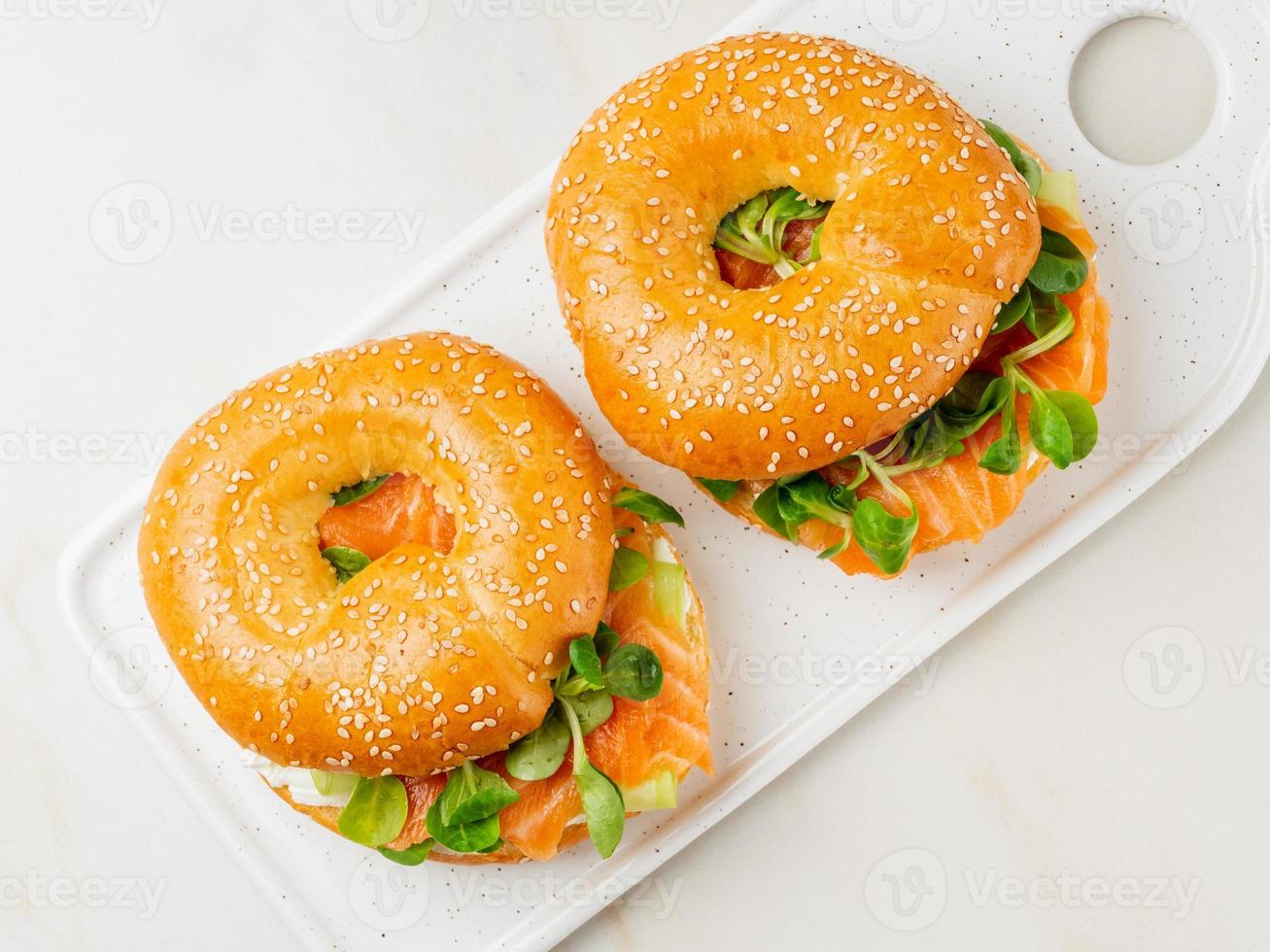 dos sándwiches con salmón, queso crema, rodajas de pepino sobre una mesa de mármol blanco foto