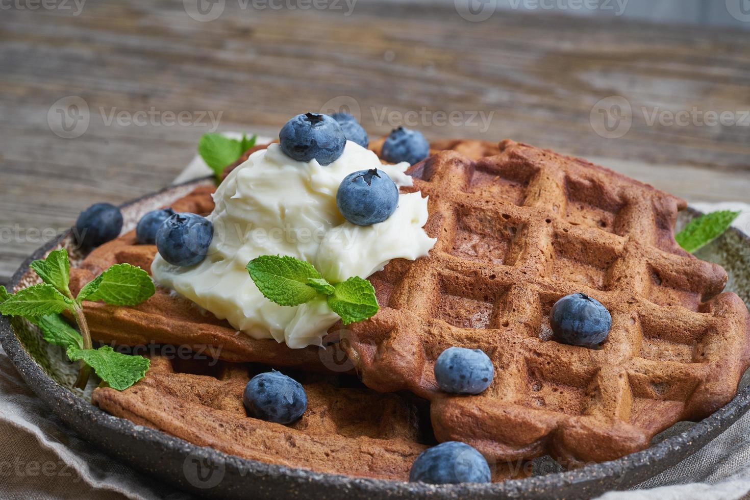 Chocolate banana waffles with blueberries, on dark wooden old table. Side view, close up photo