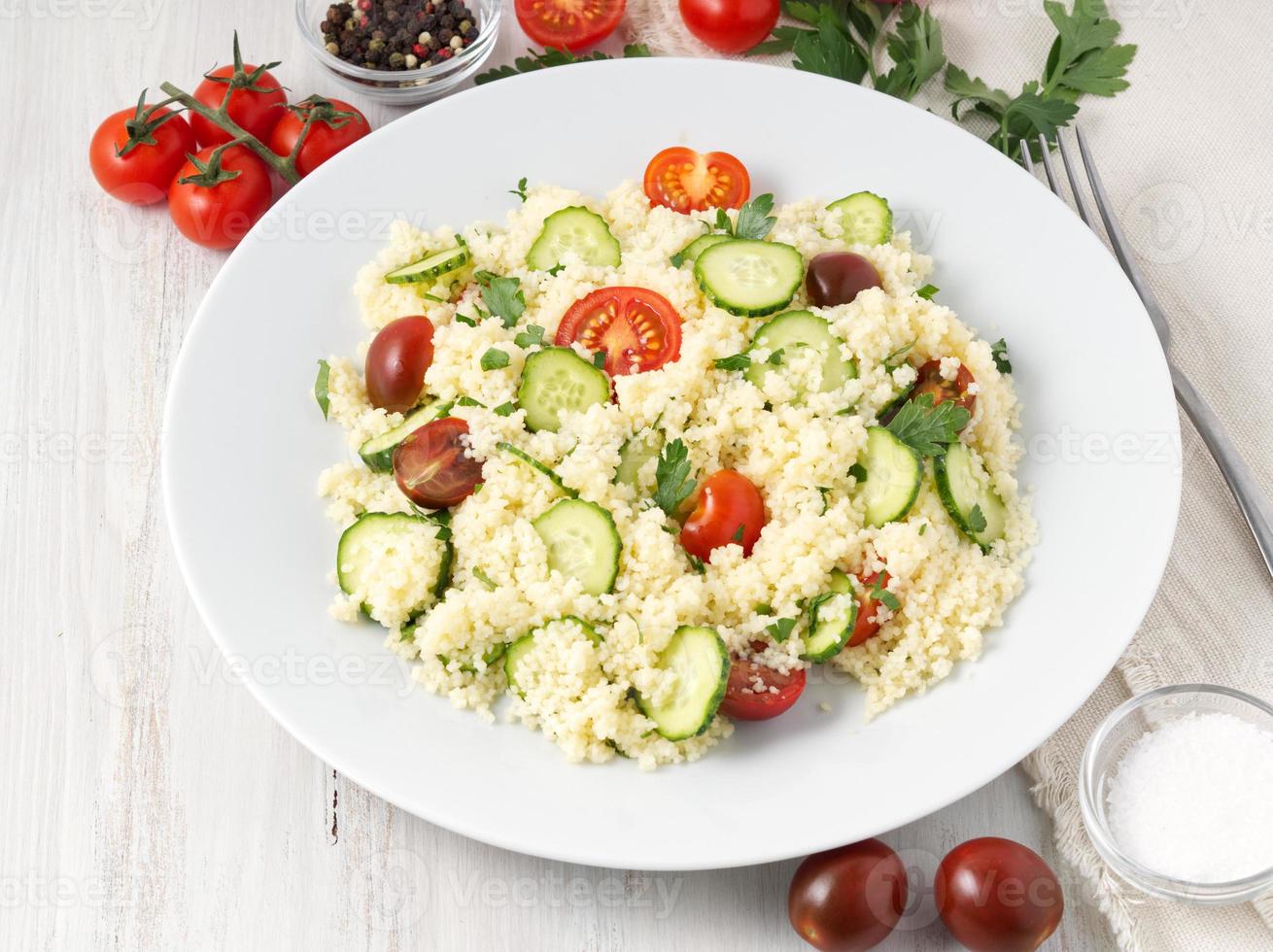 fresh diet vegetable salad with couscous, tomatoes, cucumbers, parsley, white wooden table, side view photo