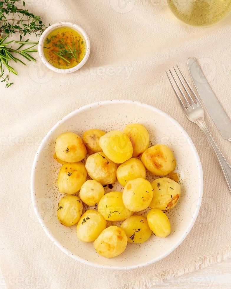 baked in oven with spices round whole potato tubers in plate on white textile background, vertical, top view photo