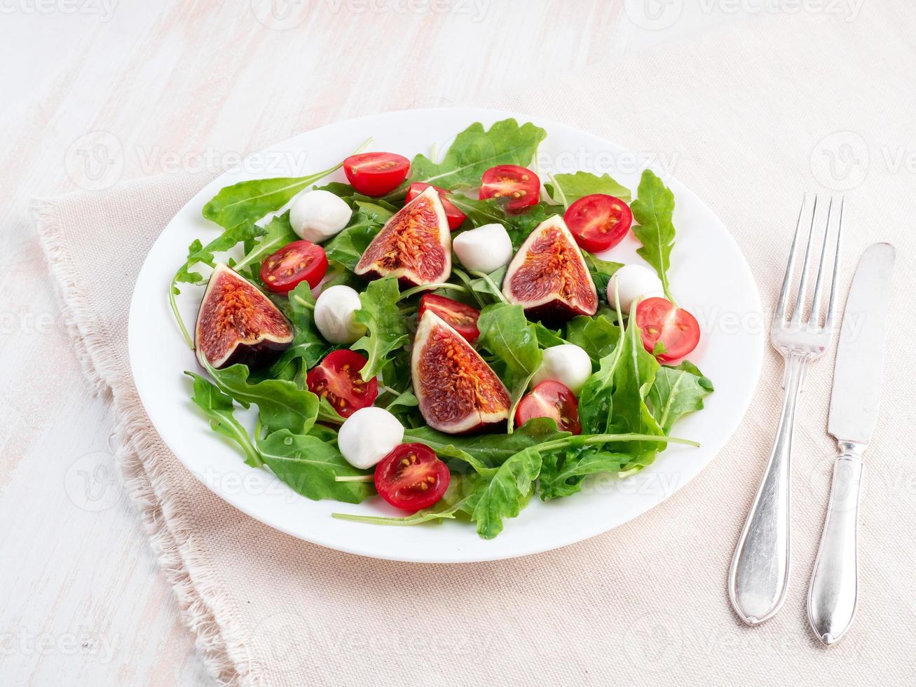 Fresh salad with figs, tomatoes, cucumbers, arugula, mozzarella. Oil with spices, side view, white background photo