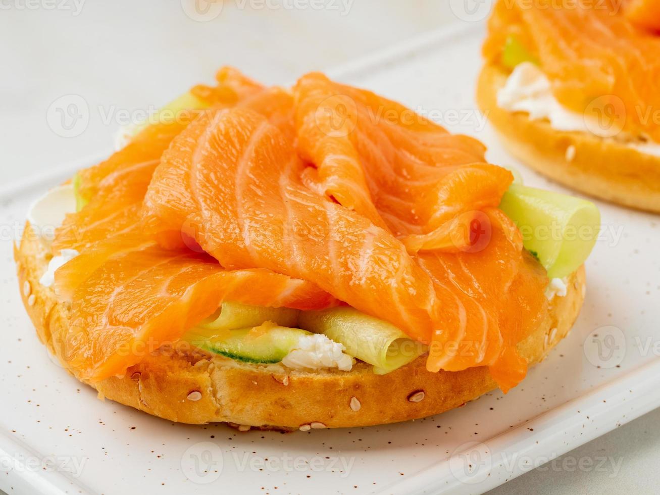 Two open sandwiches with salmon, cream cheese, cucumber slices on white marble table, close up photo