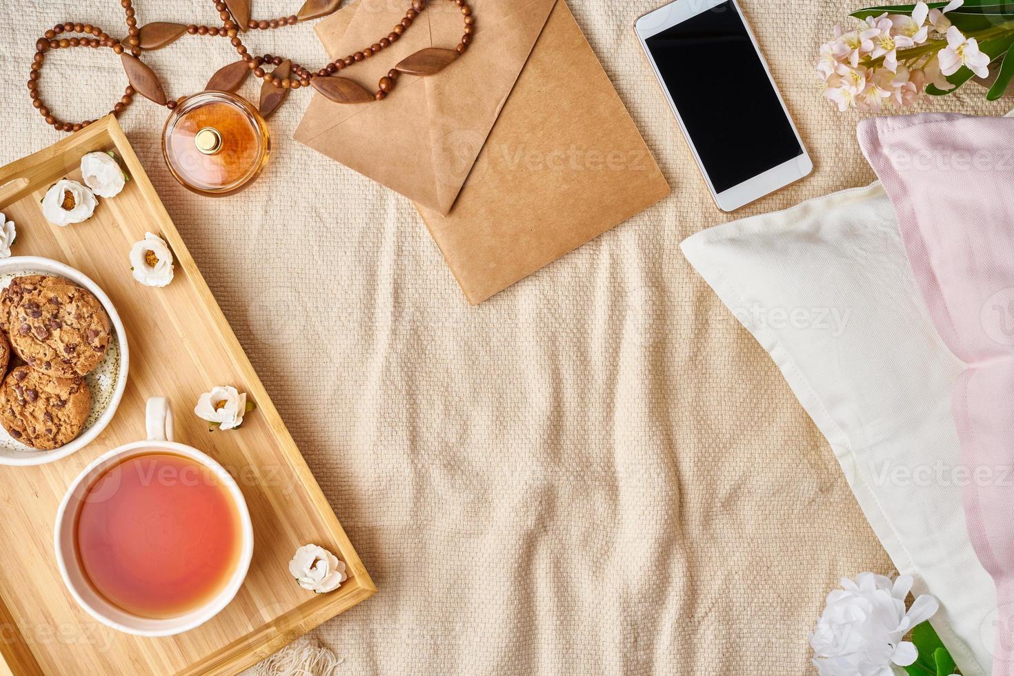 Mockup with women's accessories on bed tea, cookies, pillows, flowers, letter, notebook. photo