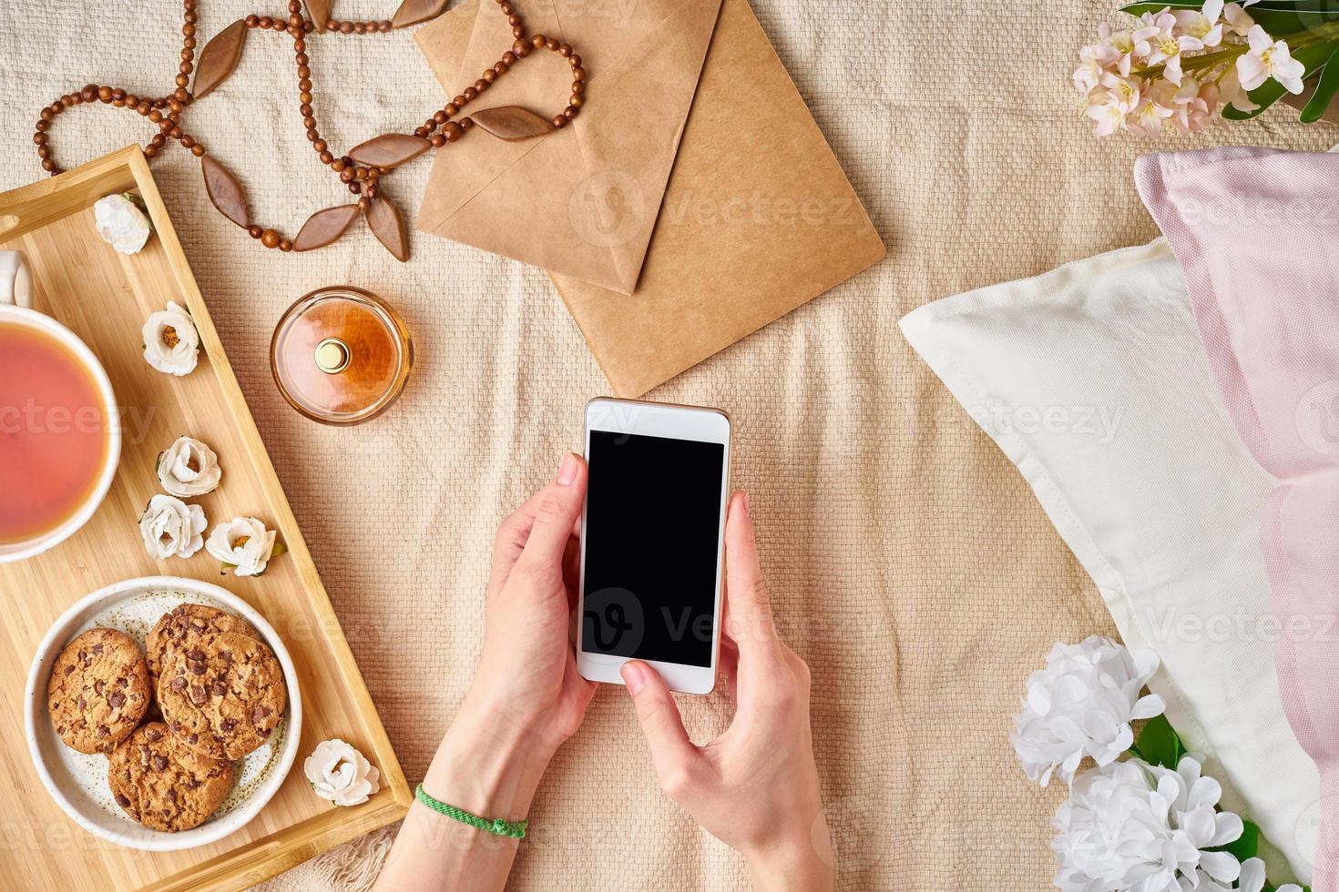 manos planas de mujeres sosteniendo un teléfono inteligente. hogar acogedor descanso, vacaciones, fin de semana. foto