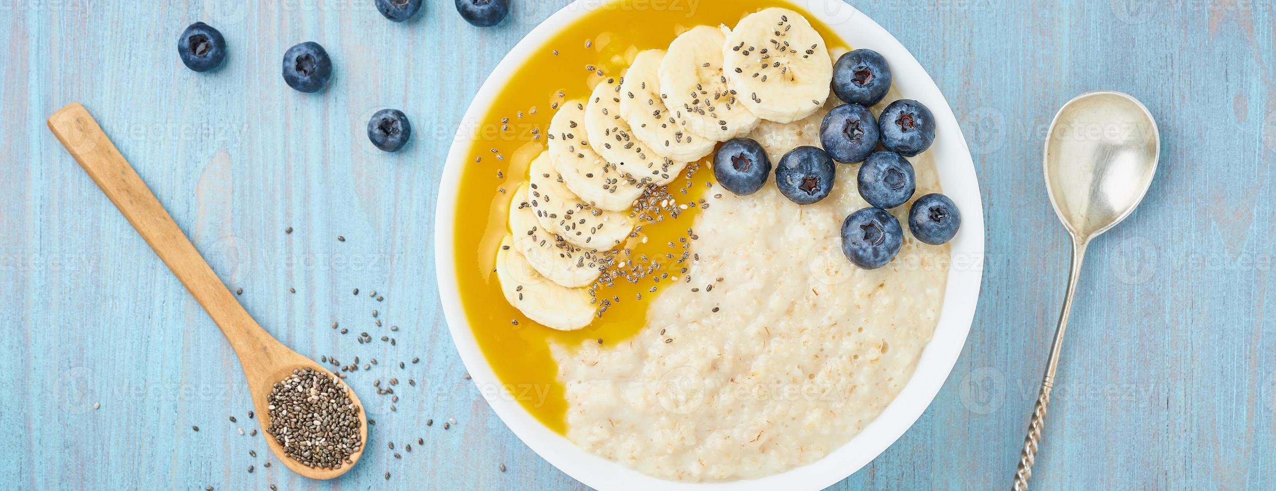 Banner with oatmeal, bananas, blueberries, chia seeds, mango jam on blue wooden background. Top view. Healthy breakfast. photo