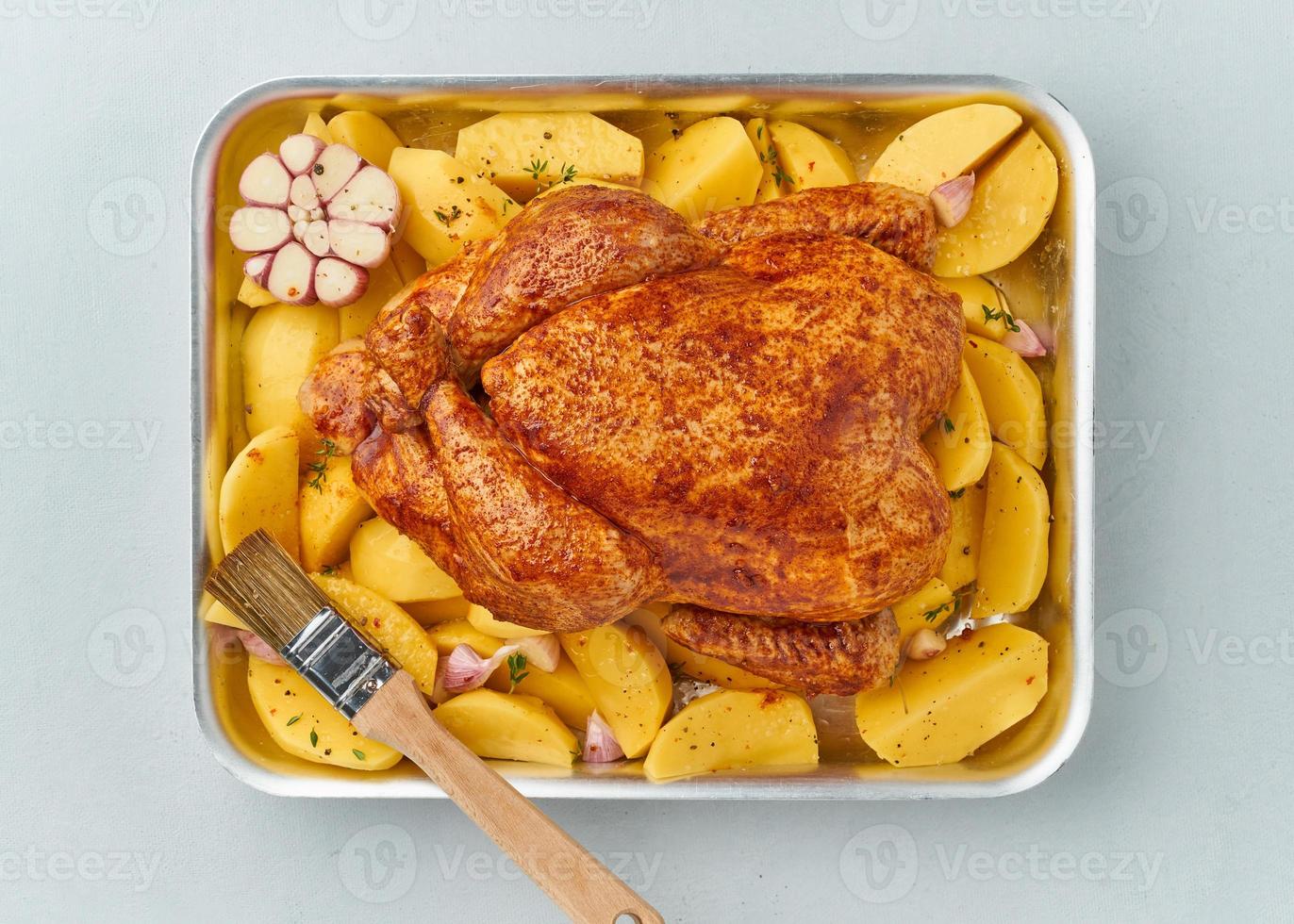 pollo entero marinado en salsa con patatas crudas, con pincel en una fuente para horno, vista superior. foto