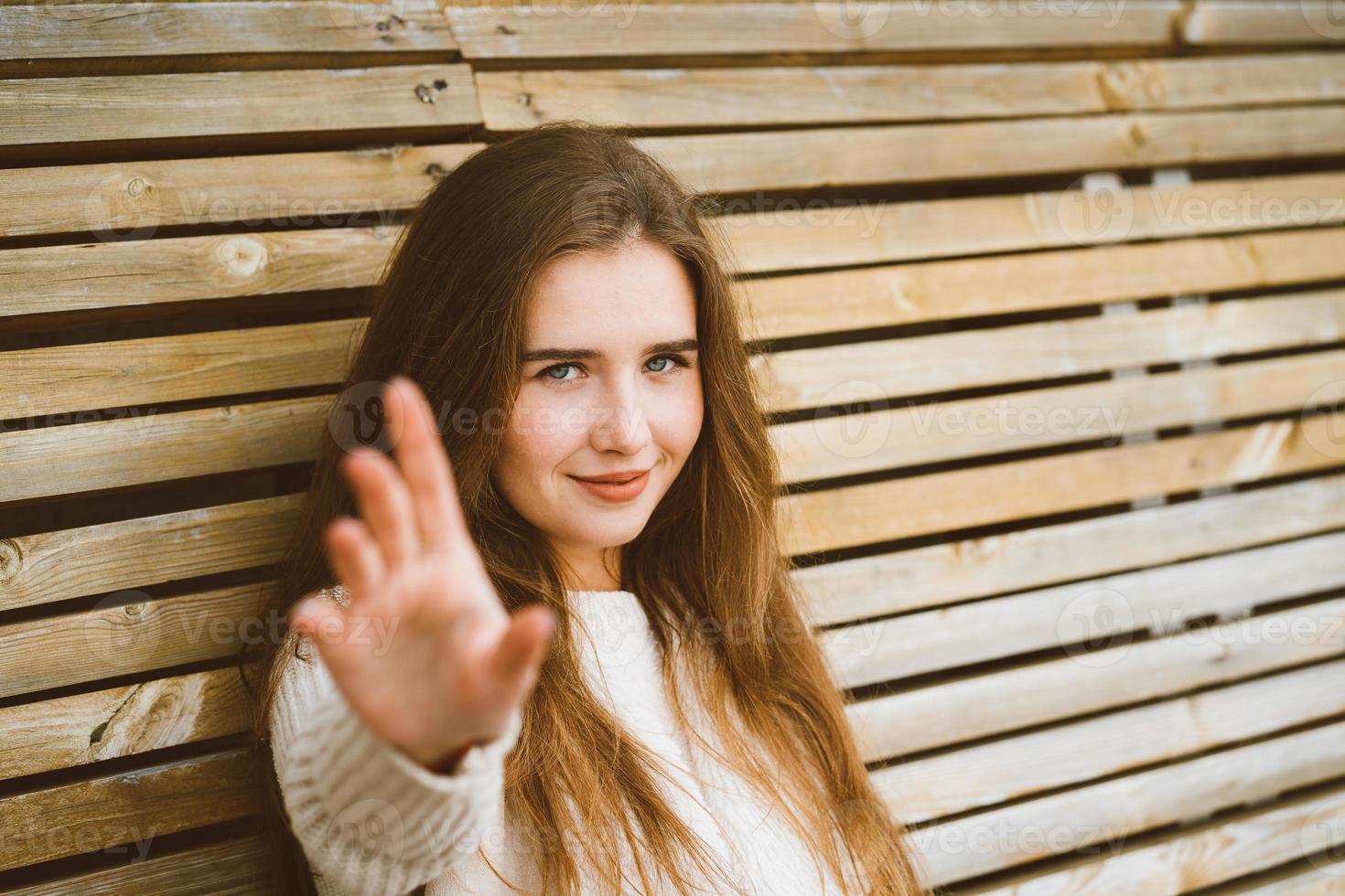 bella joven con el pelo largo estira la mano hacia la cámara, mujer caucásica sentada en un banco de madera y tirando de los brazos, espacio vacío para el texto foto