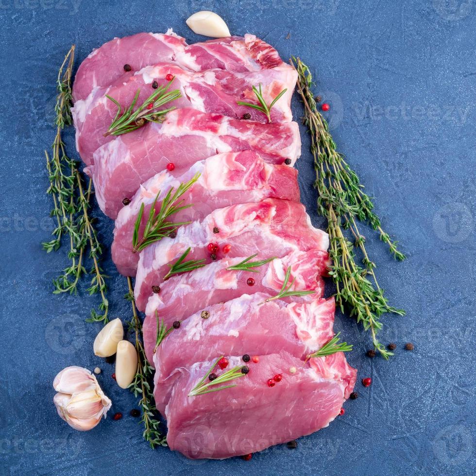 Pork steak, raw carbonate fillet on dark background, meat with rosemary, garlic seasonings, top view photo